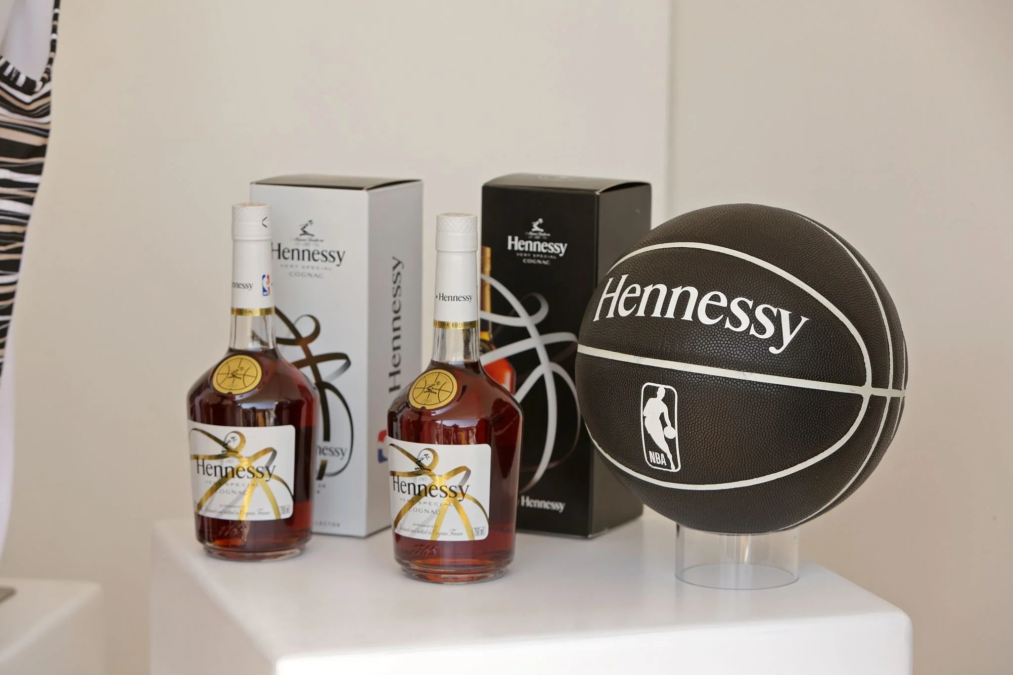 Two bottles of Hennessy cognac, two boxed packages of Hennessy, and a Hennessy NBA basketball on display on a white surface.