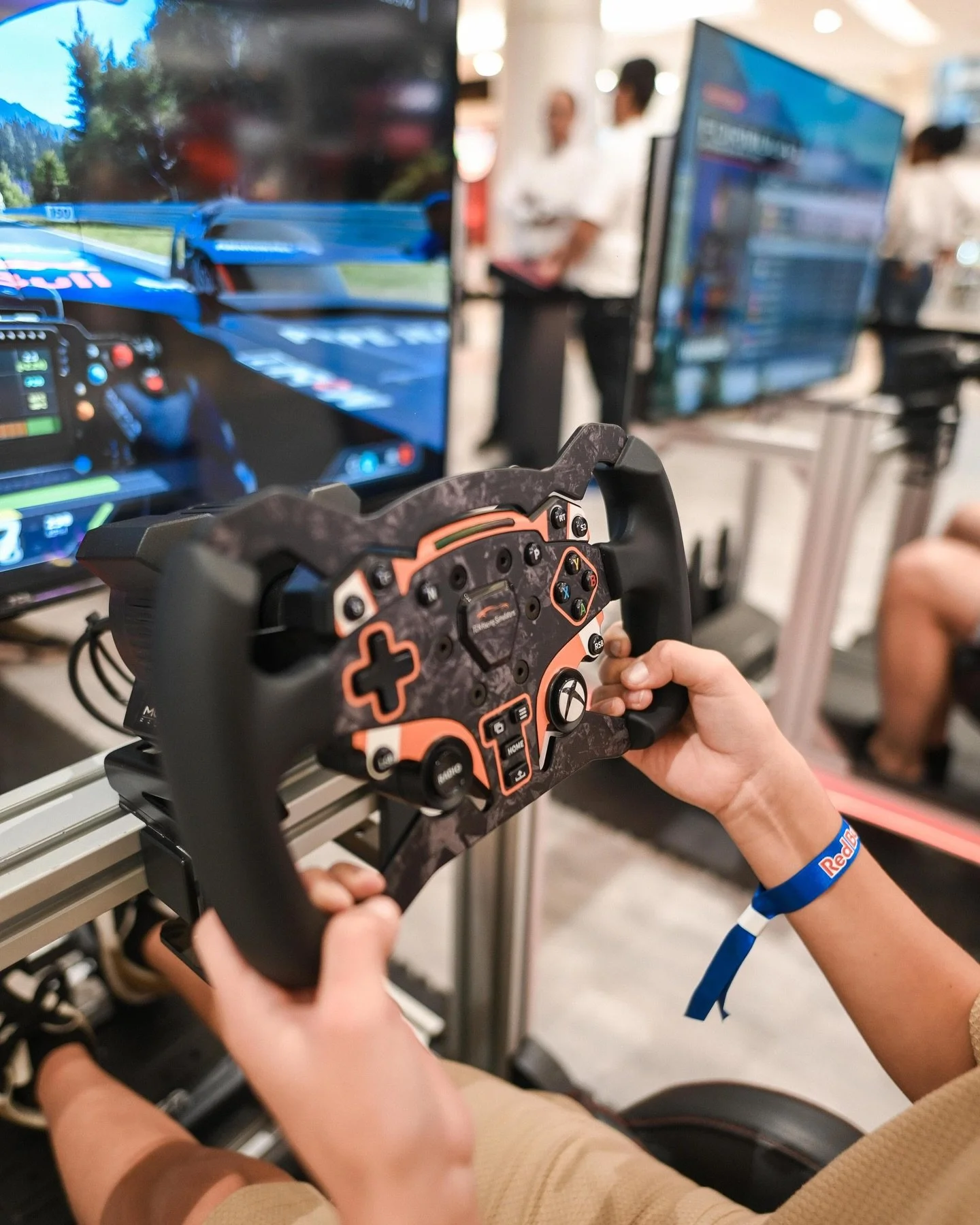 A person holding a racing wheel controller in front of a racing simulator screen at an event or store.