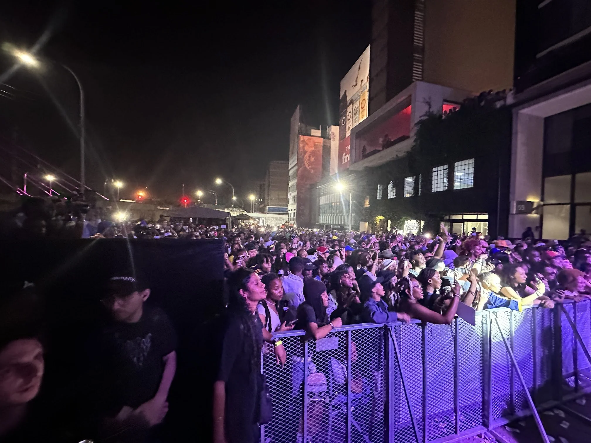 Crowd of people gathered outside at night near a building with bright lights and large advertisement banners.