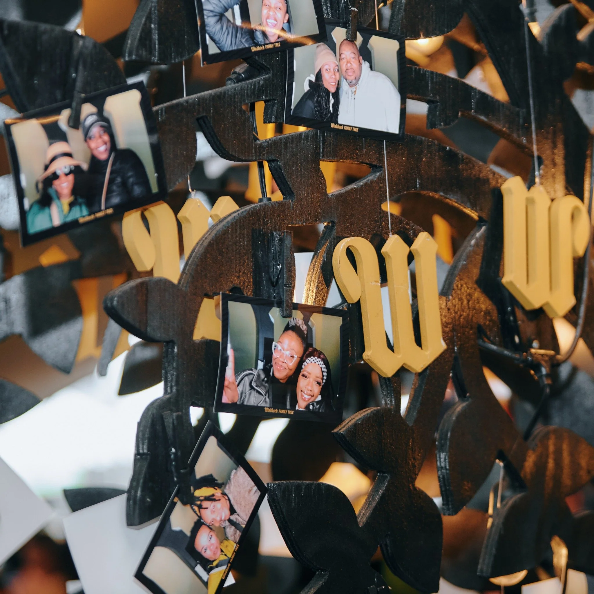 A decorative photo display featuring several printed photos of diverse people, hanging on a black and yellow themed background with gold-colored letters spelling 'W' and 'U'.
