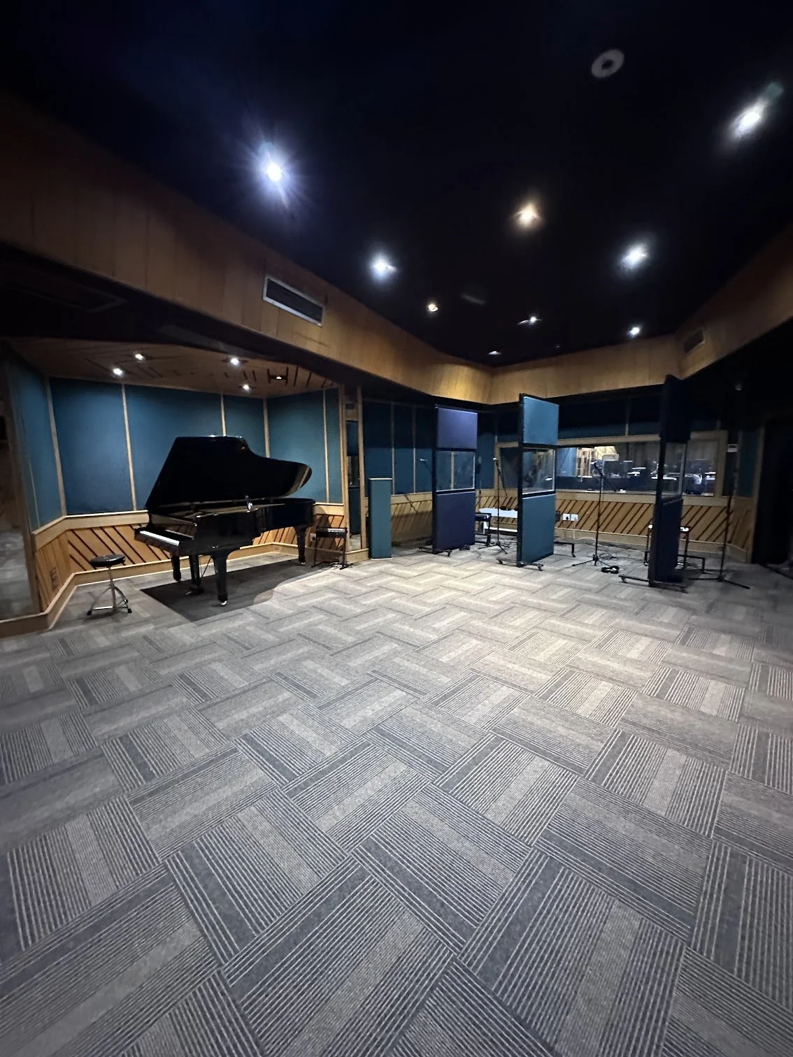 Empty recording studio with a grand piano, several music stands, microphone stands, and acoustic panels.