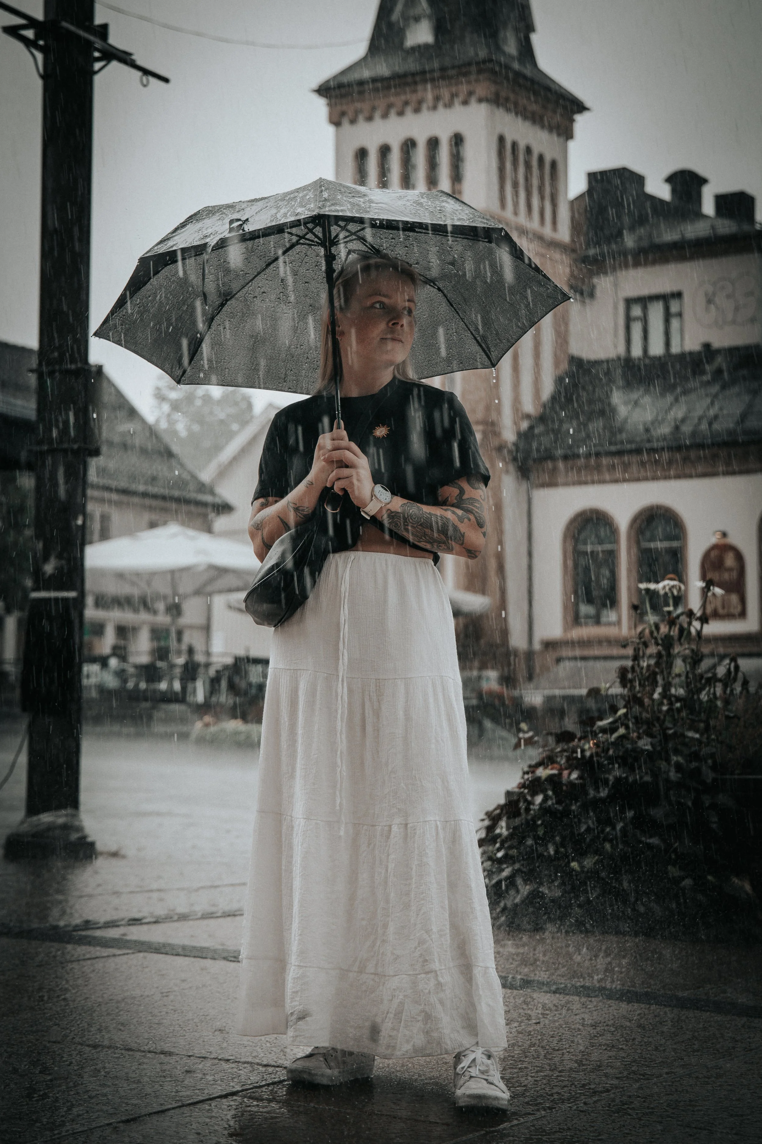 Kvinne med paraply står i regnet foran en kirke i en liten by. Mitt i Tønsberg sentrum.