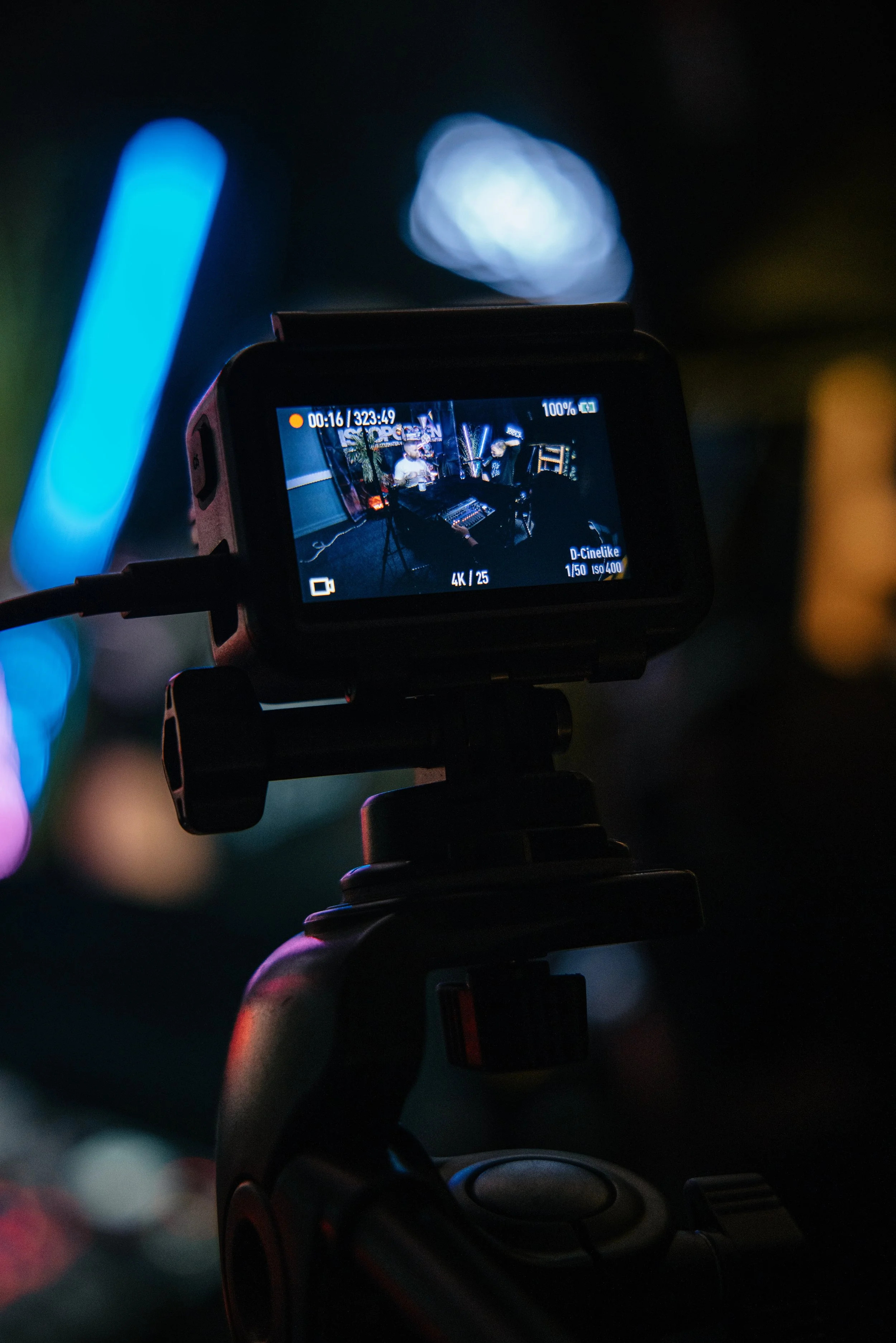 Et kamerahode viser en innendørs scene med to personer som sitter foran en mikserbord, omgitt av lysutstyr.