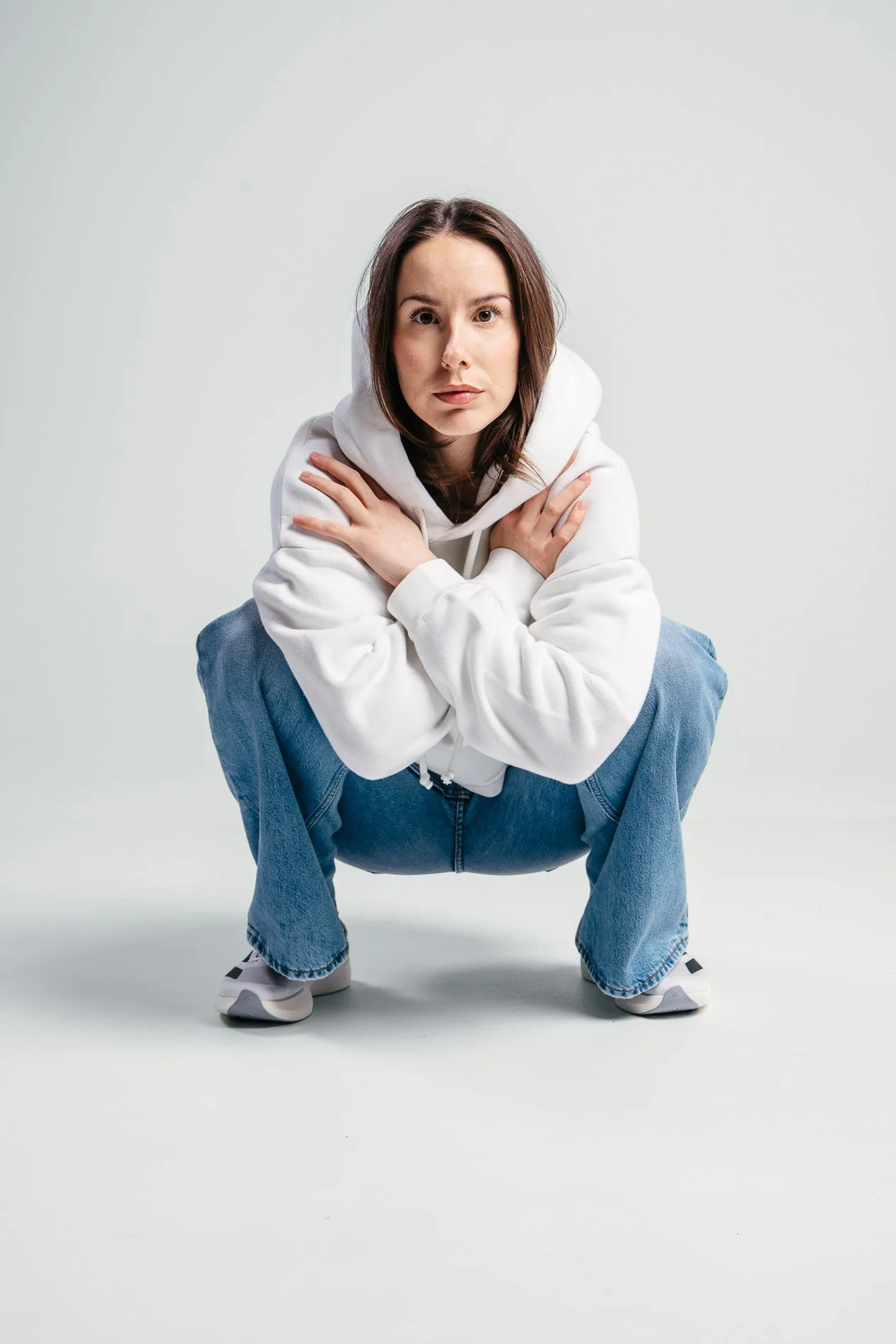 En kvinne i hvit sweatshirt og blå jeans i en lav knebøyposisjon mot en enkel lys bakgrunn.