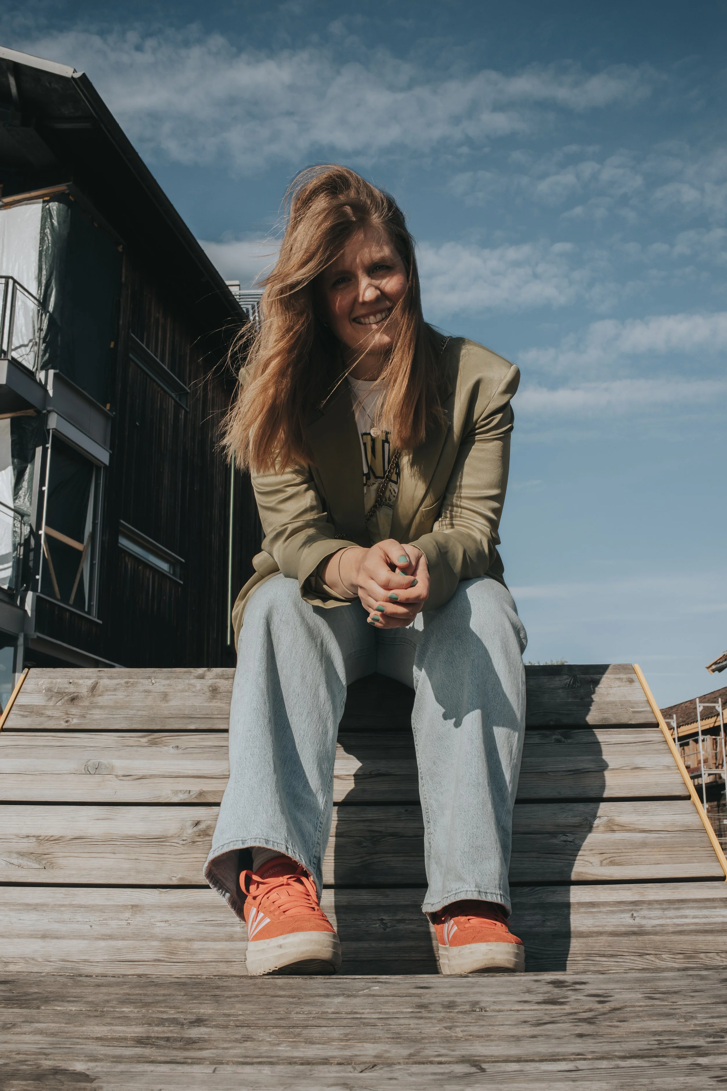 Ung kvinne som sitter på en treplattform utendørs under en klar himmel.