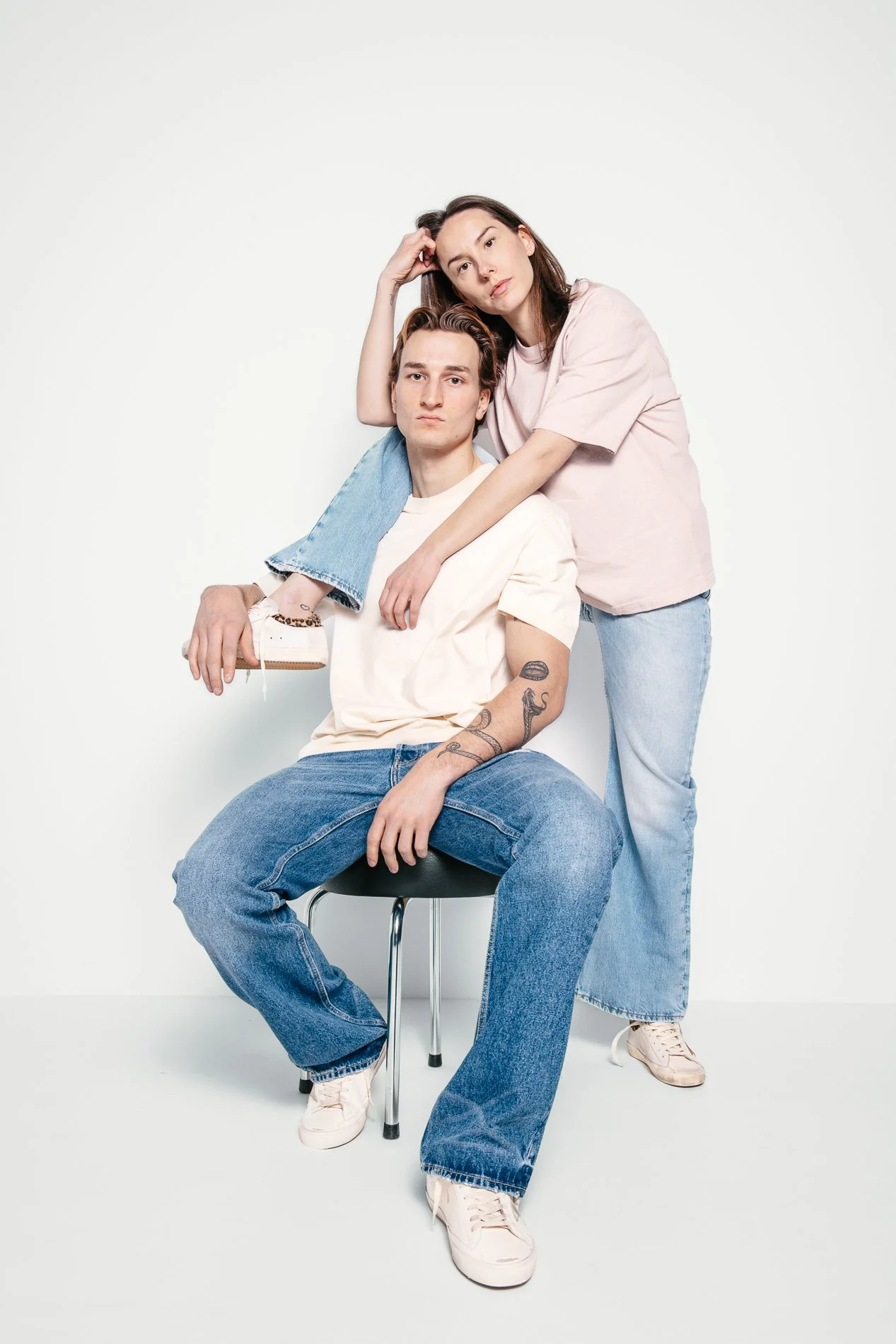 To personer poserer mot en hvit bakgrunn, en mann sitter på en stol med en kvinne som står bak ham med armen rundt ham og hodet hvilende på hennes hånd.