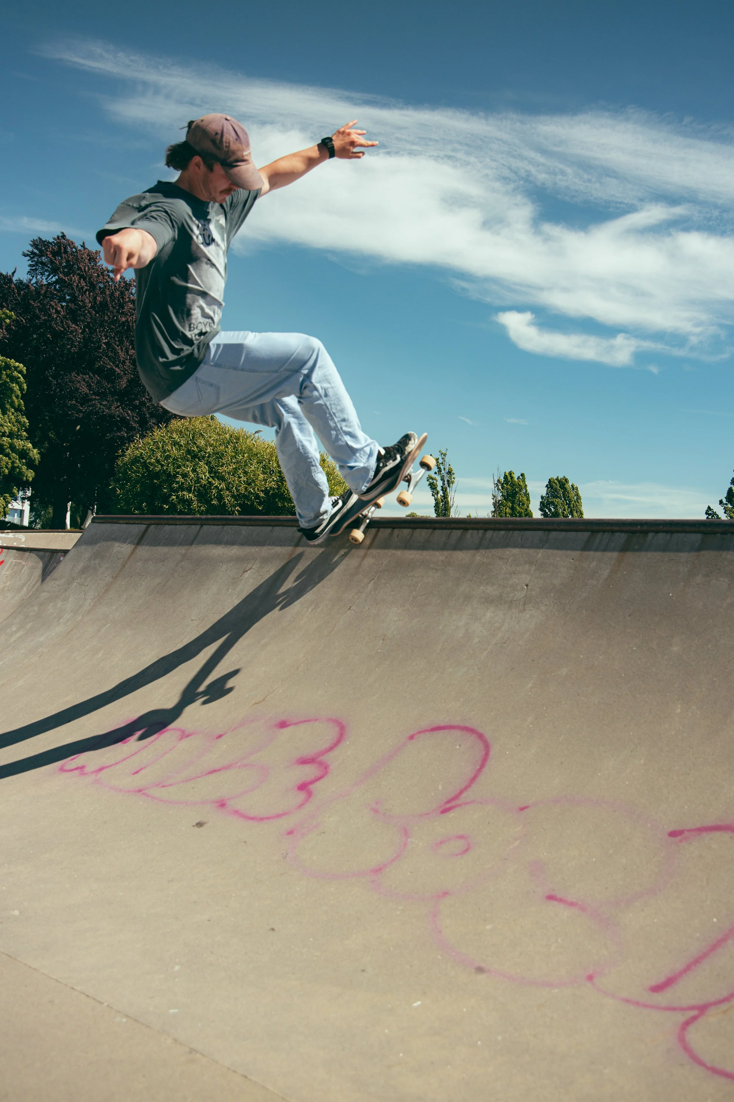 En person som skateboarder utfører et trick på en skatepark under en blå himmel med skyer.