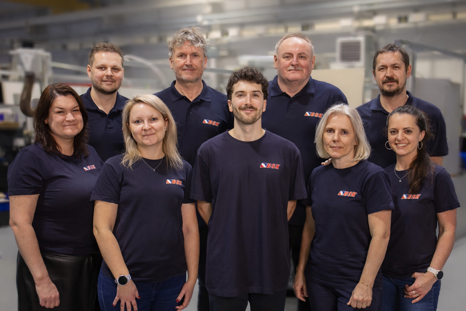 Eine Gruppe von neun Menschen in blauem Arbeitskleidung mit dem Logo 'BSK' steht in einer Fabrikhalle.