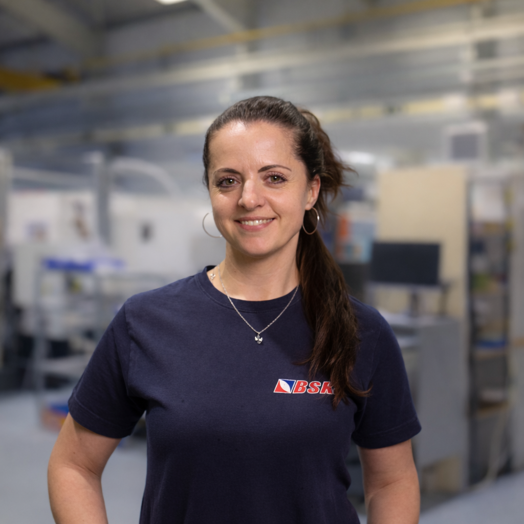 Eine Frau mit dunklem Haar, die eine dunkelblaue BSH-T-Shirt trägt, steht in einer Industrie- oder Lagerhalle.
