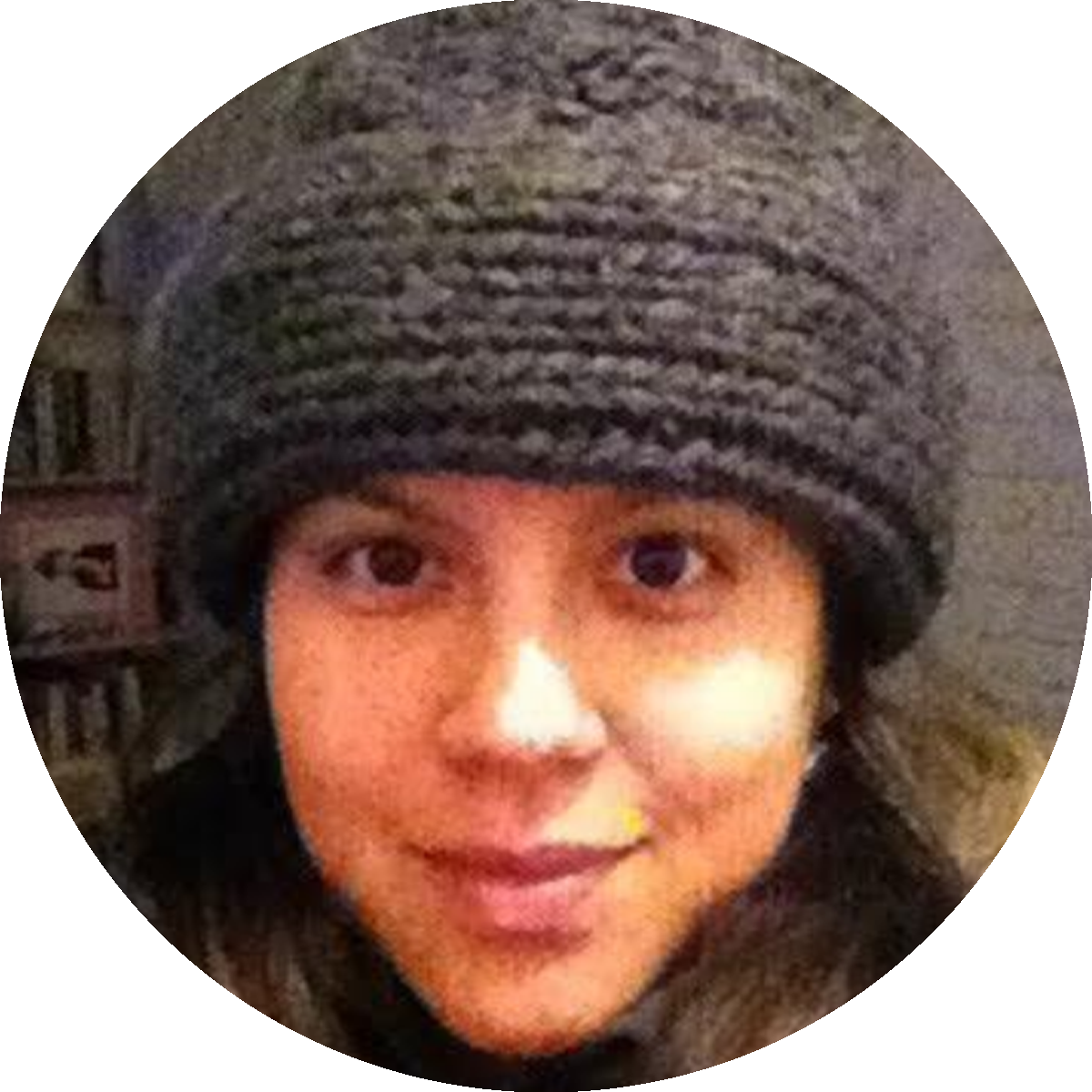 Retrato de uma criança com pele clara, usando um gorro cinza com listras e um casaco com capuz. Fundo desfocado com elementos de móveis.