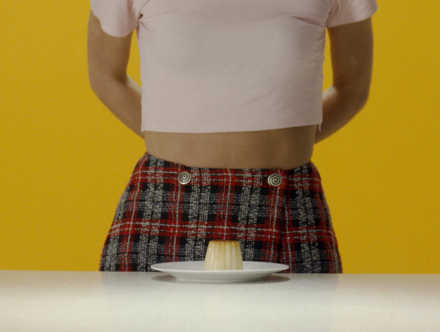 Person standing behind table with a flan on a white plate, yellow background