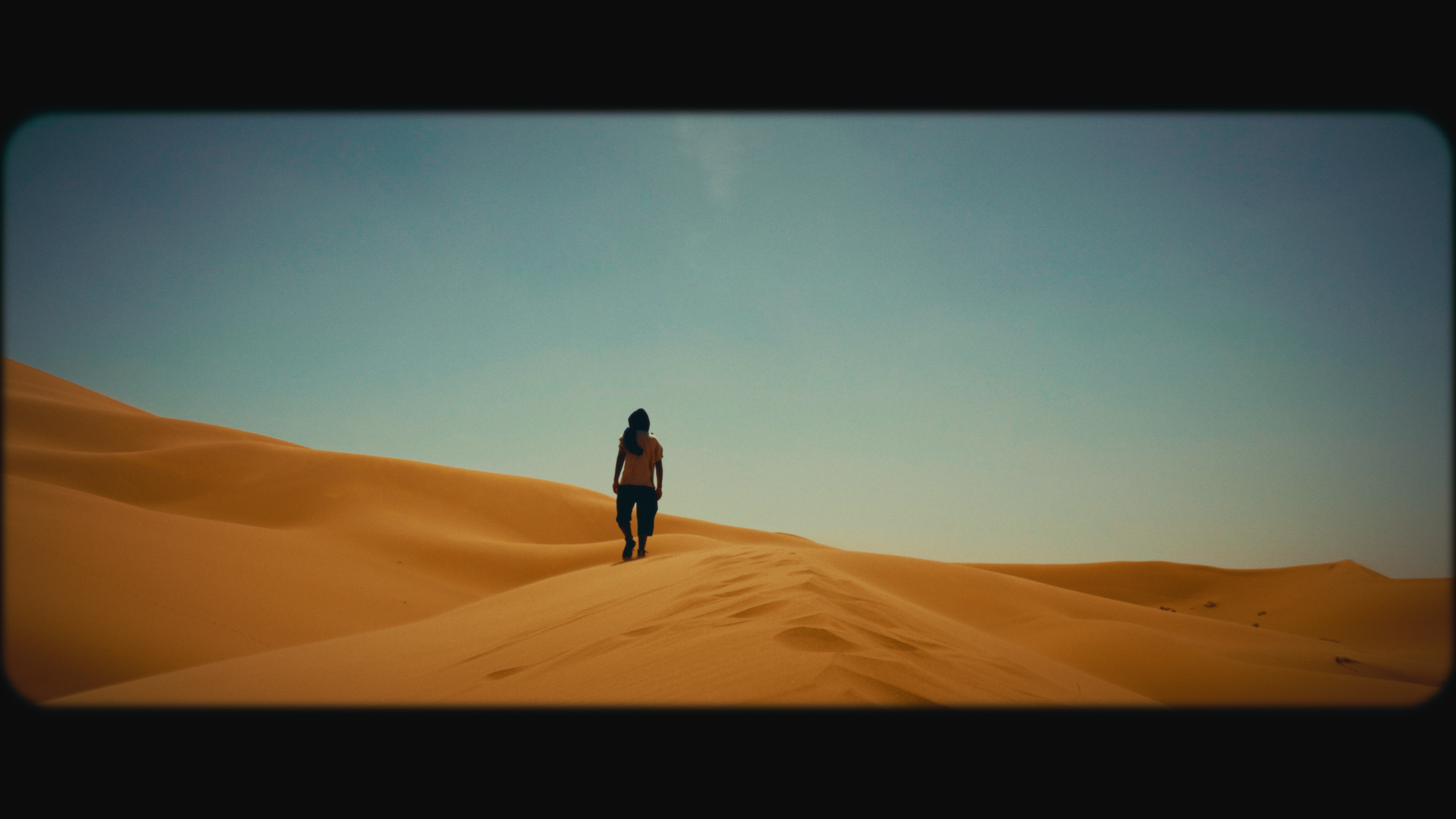 A person walking alone through sandy desert dunes under a clear blue sky.