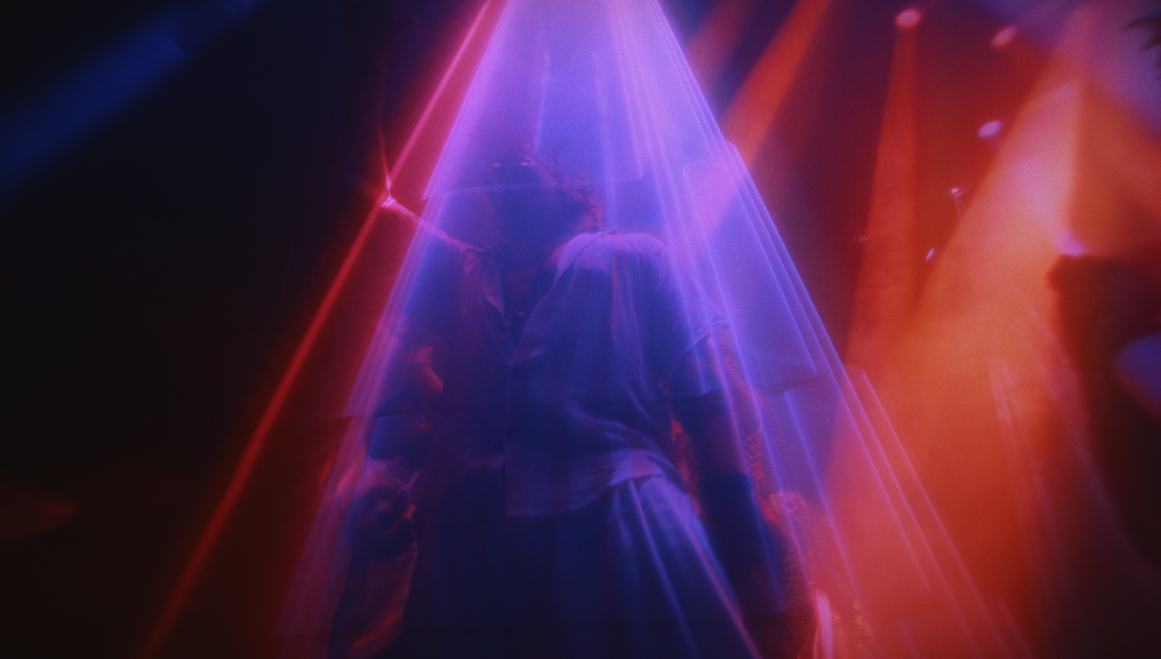 A person standing under colorful neon lights, with purple and red light beams creating an atmospheric, glowing effect.