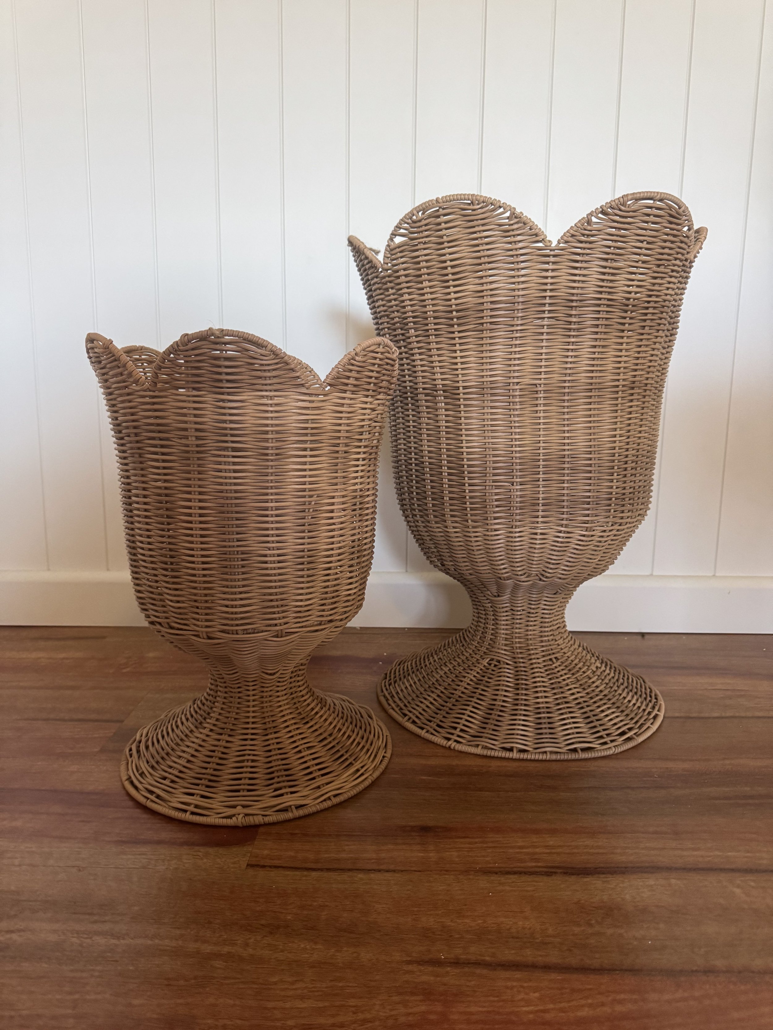 Two decorative wicker vases, one larger and one smaller, placed on a wooden surface against a white wall.