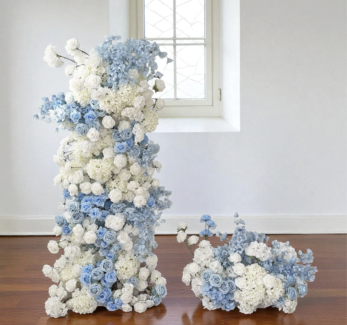 Arrangements of white and light blue flowers, with some flowers resting on the wooden floor near a white wall and window.