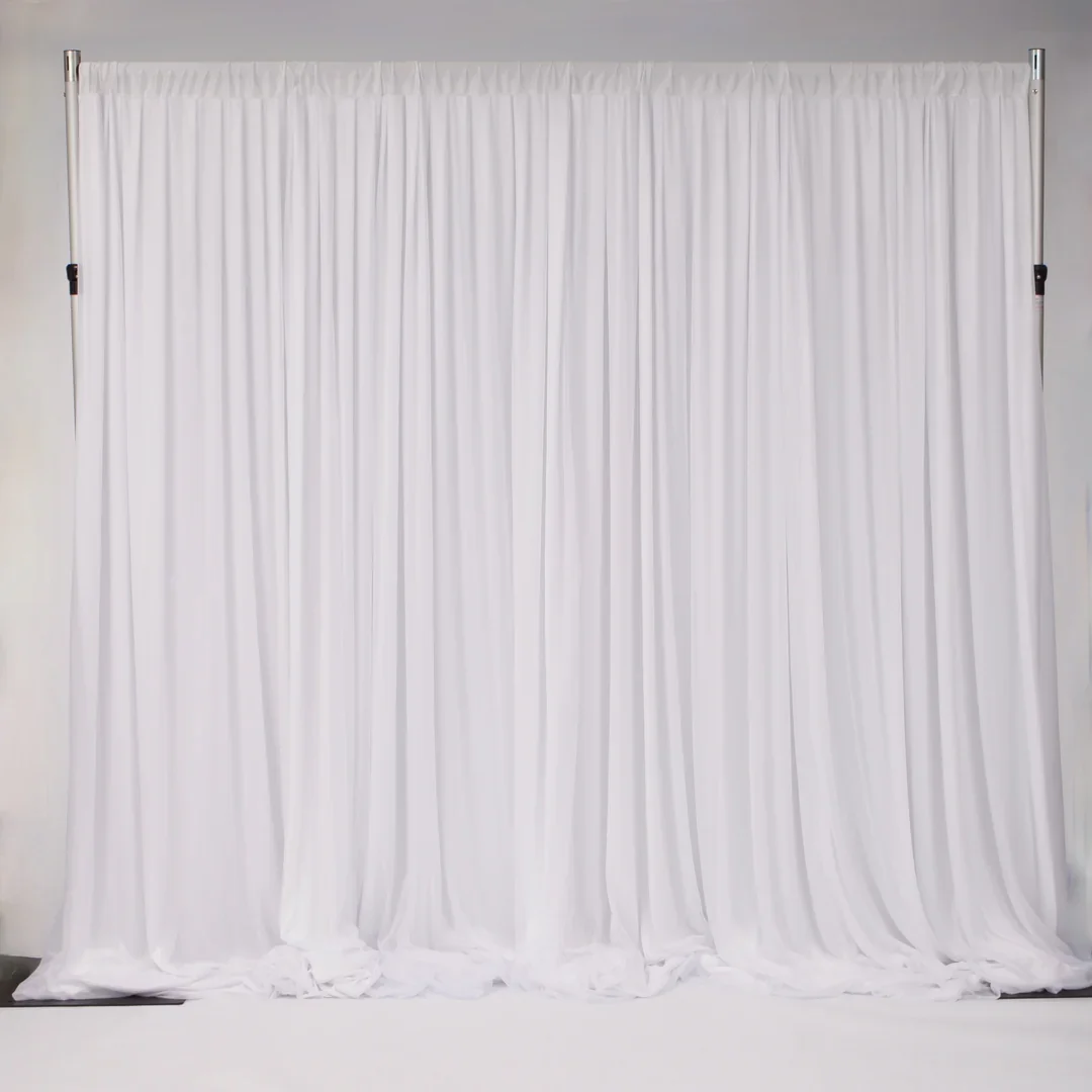 A large white fabric backdrop with gathered curtains hanging from a metal frame in front of a plain wall.