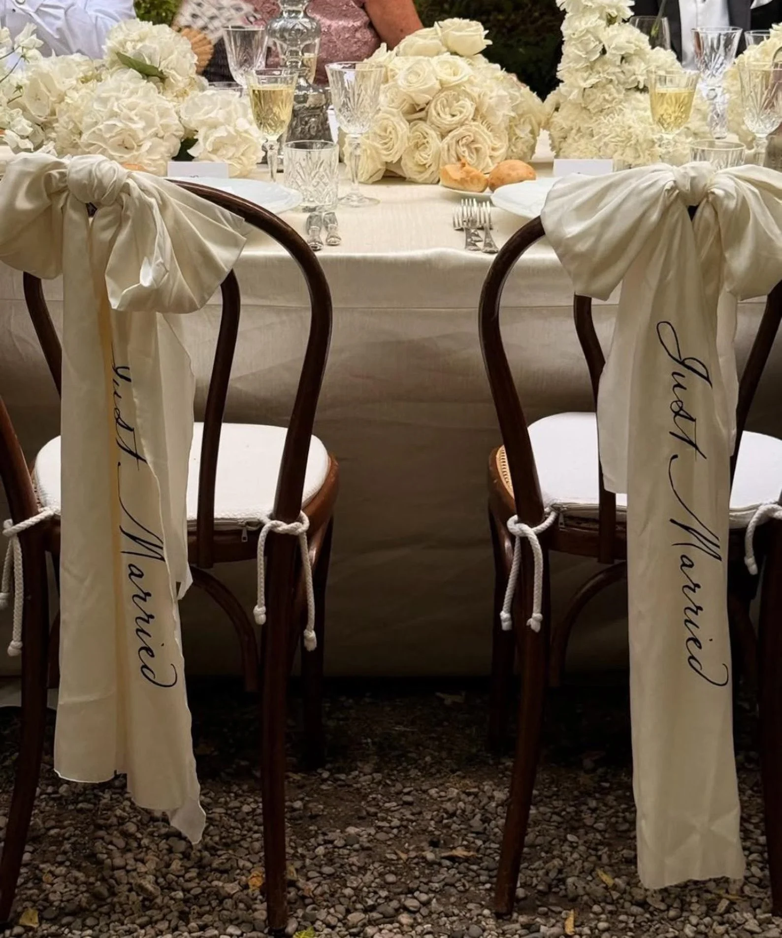 Decorated dining table with floral arrangements, glasses of champagne, and chairs with white ribbons labeled 'Guest Married'.