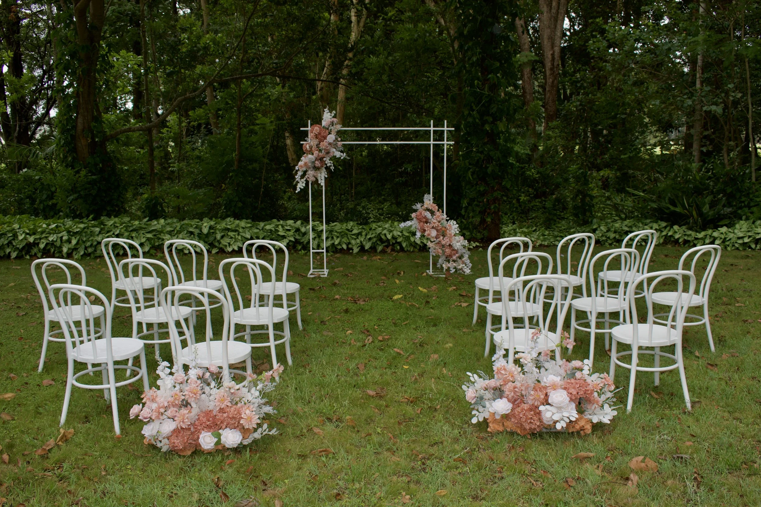 A wedding arch decorated with pink, peach, white, and cream flowers alongside flowing beige and cream drapes, set against a plain white wall.