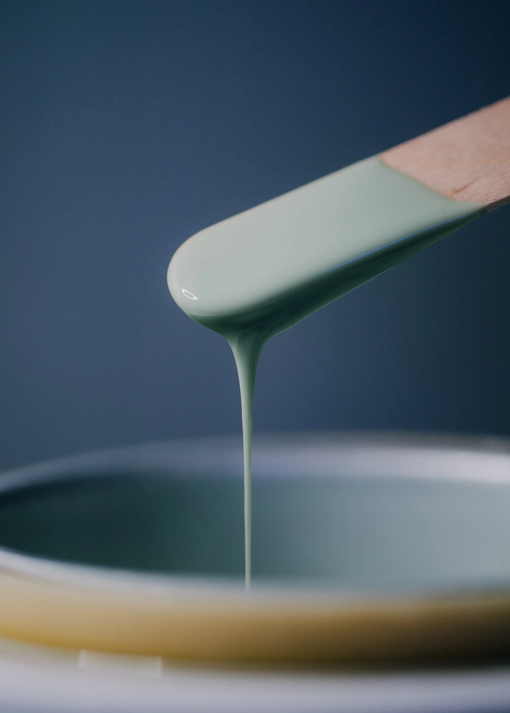Close-up of a spatula lifting a dollop of light green sauce or batter over a bowl.
