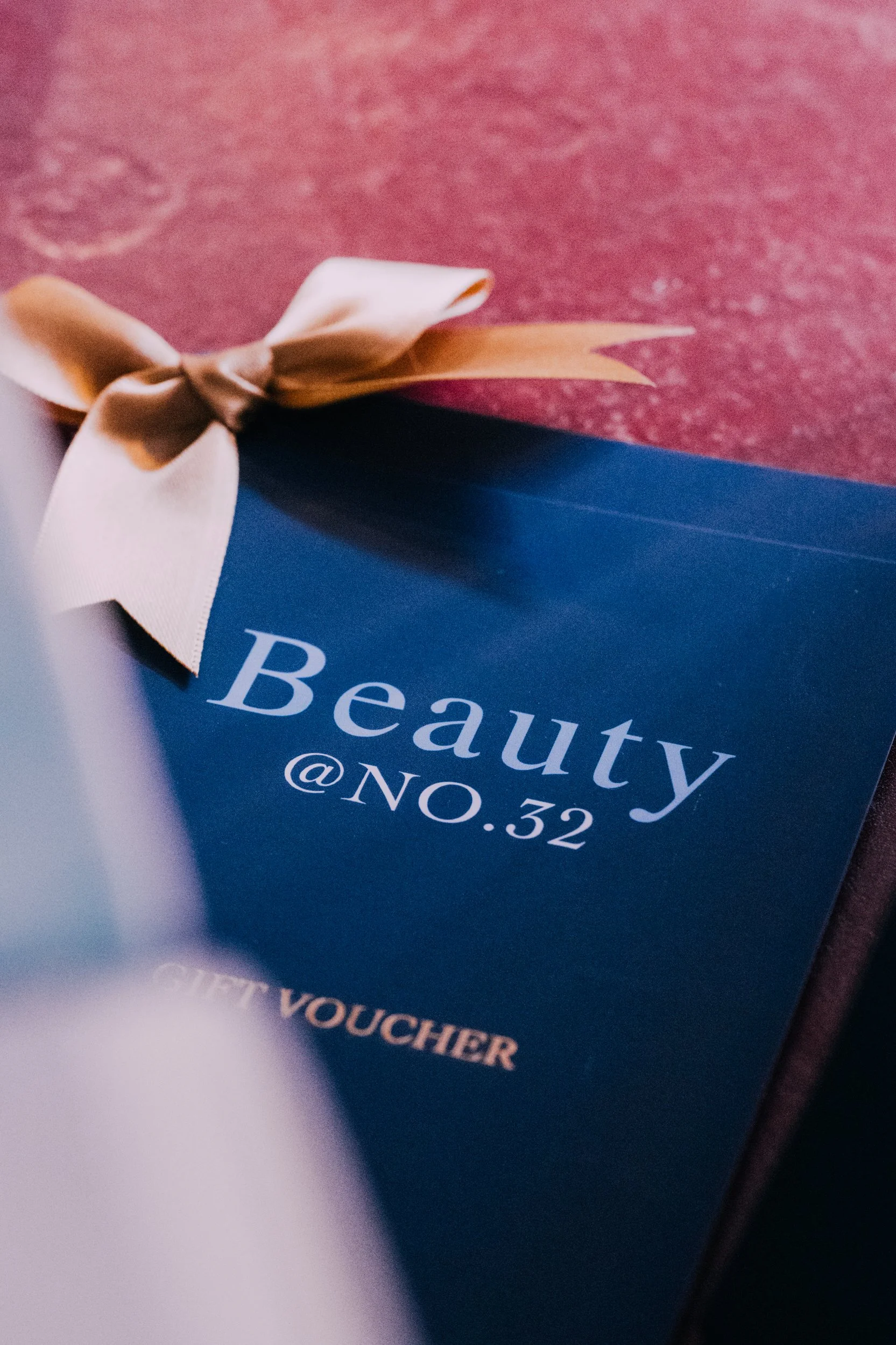 A blue beauty gift voucher with a beige ribbon tied in a bow, placed on a red surface.