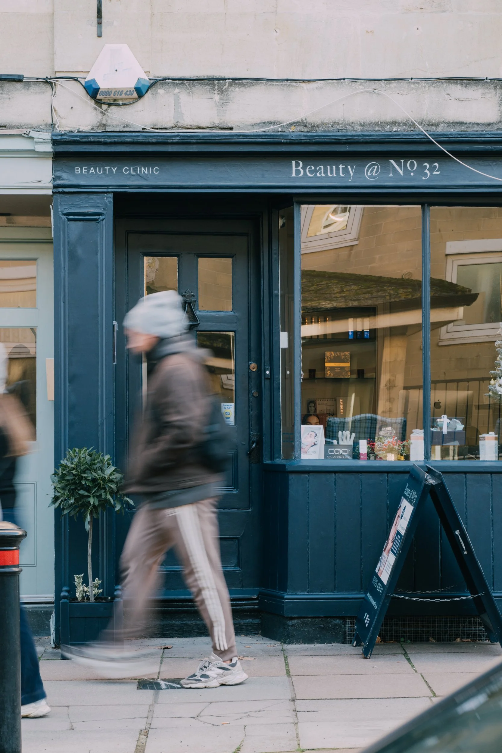 Blurred person walking past the exterior of a beauty clinic with a dark blue storefront.