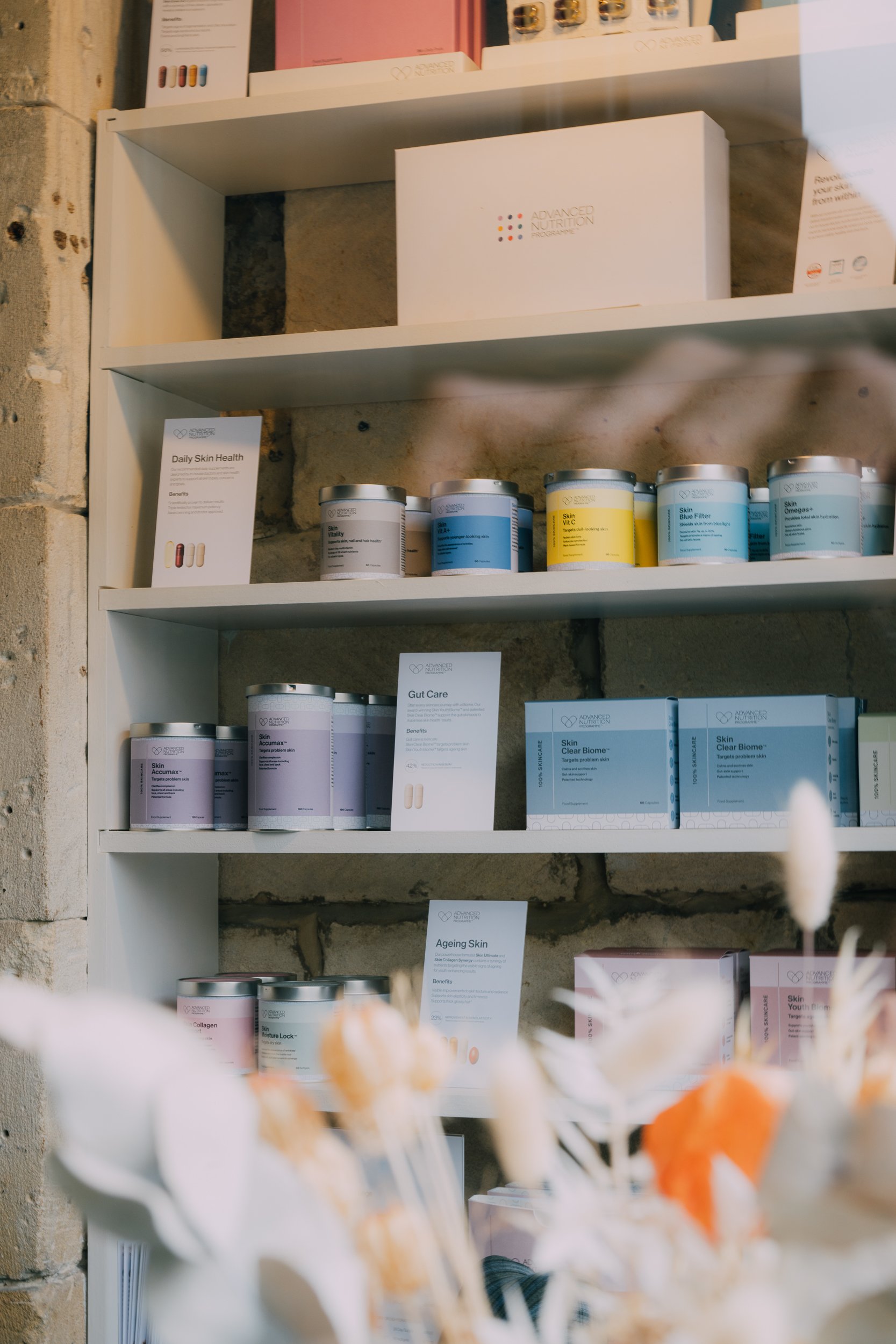 Shelves displaying various health and skincare products from Advanced Nutrition Programme, including supplements for skin health, gut care, and aging skin, with informational signs.