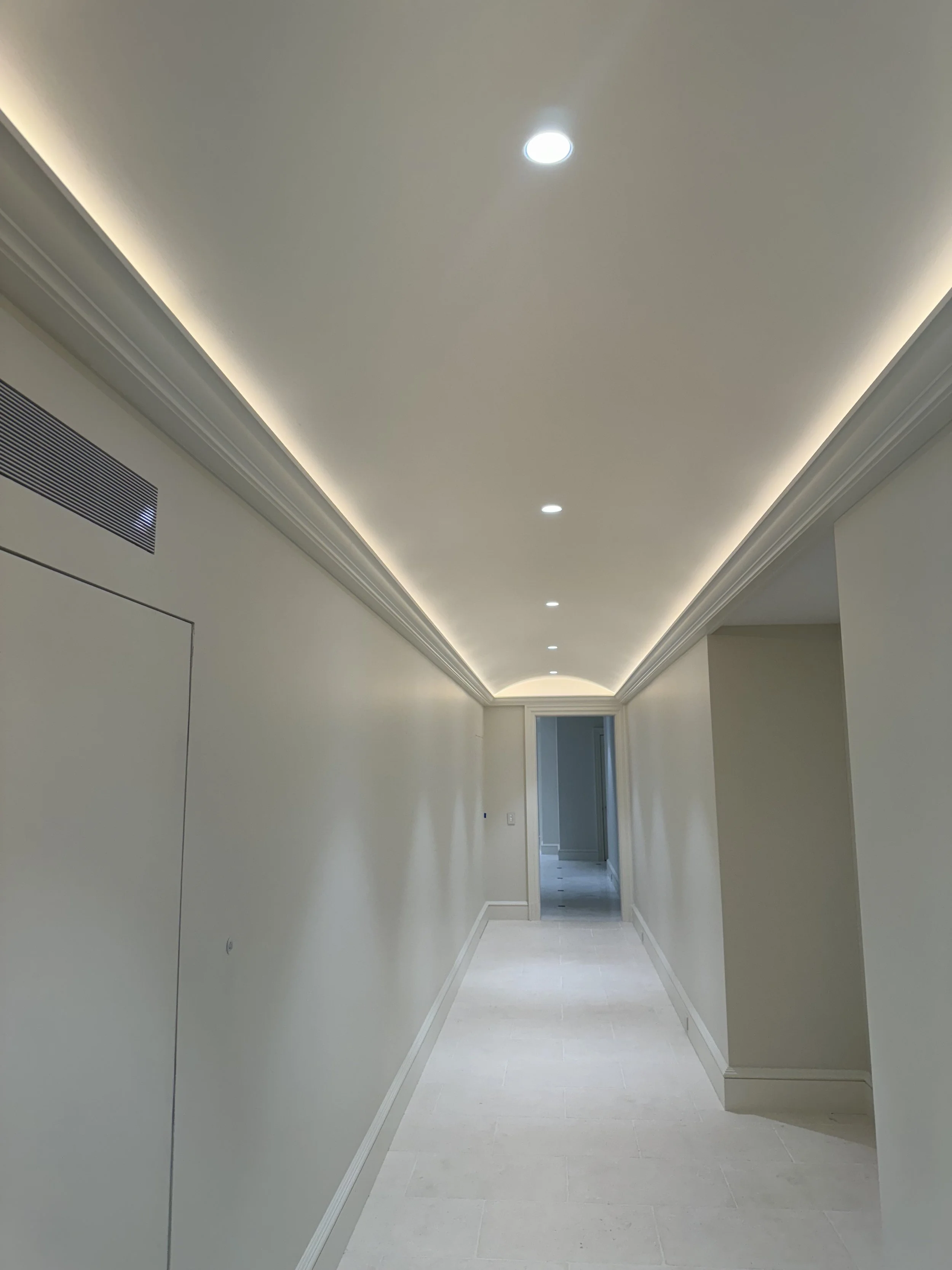 Empty hallway with white walls, ceiling lighting, and a doorway at the end.