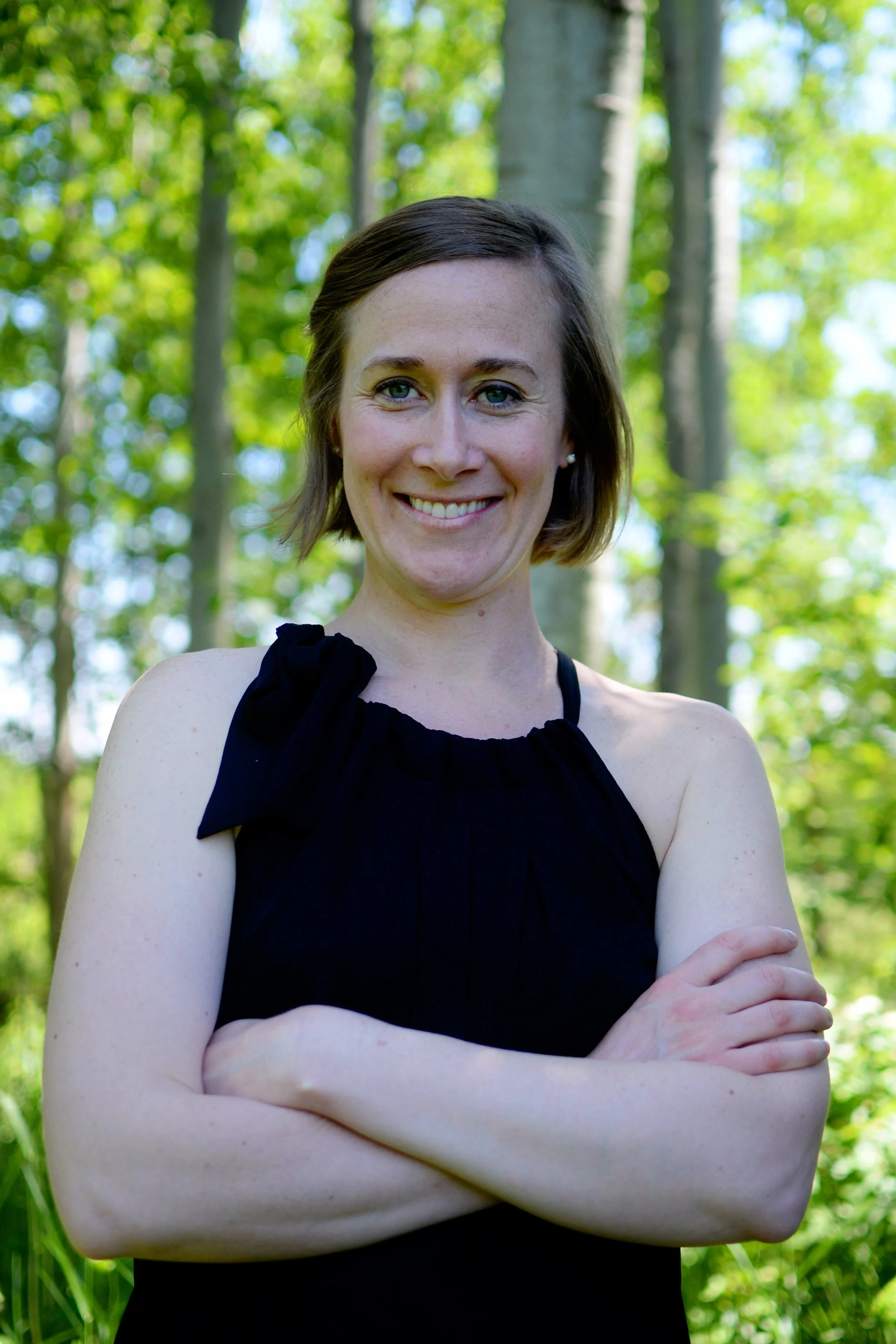 Lara Desrosiers of Pelvic Resilience smiling outdoors in a forest, wearing a black sleeveless top, arms crossed. She is the owner of Pelvic Resilience and provides continuing education, mentorship, and resources to occupational therapists.