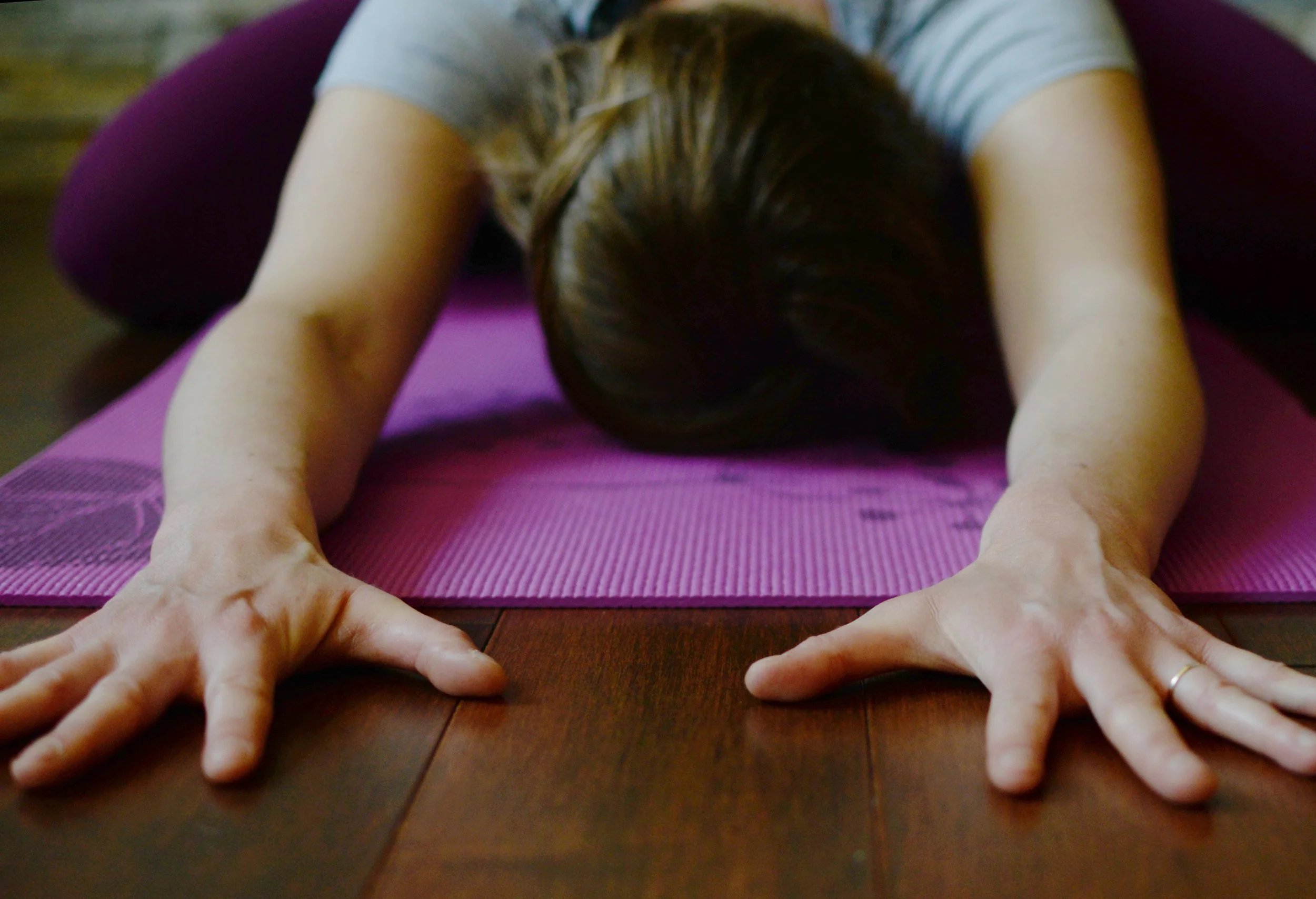 Lara Desrosiers of Pelvic Resilience practicing yoga in child's pose on a purple mat, extending arms forward on wooden floor. She is the owner of Pelvic Resilience and provides continuing education, mentorship, and resources to occupational therapist