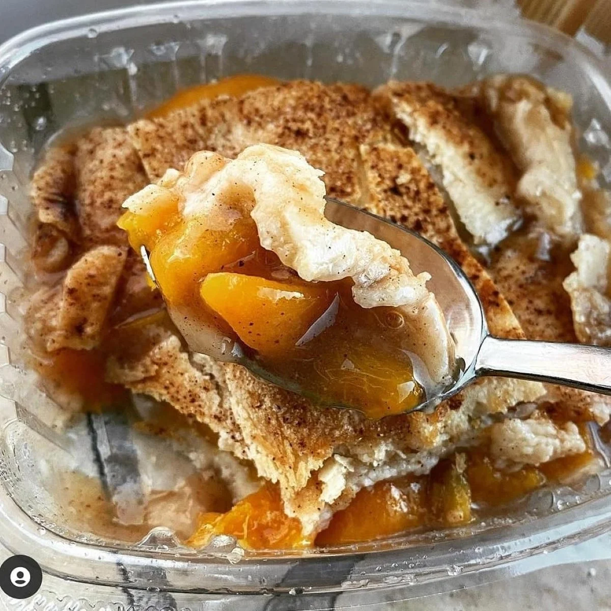 A spoonful of peach cobbler with peach filling and crumbly topping in a dish.
