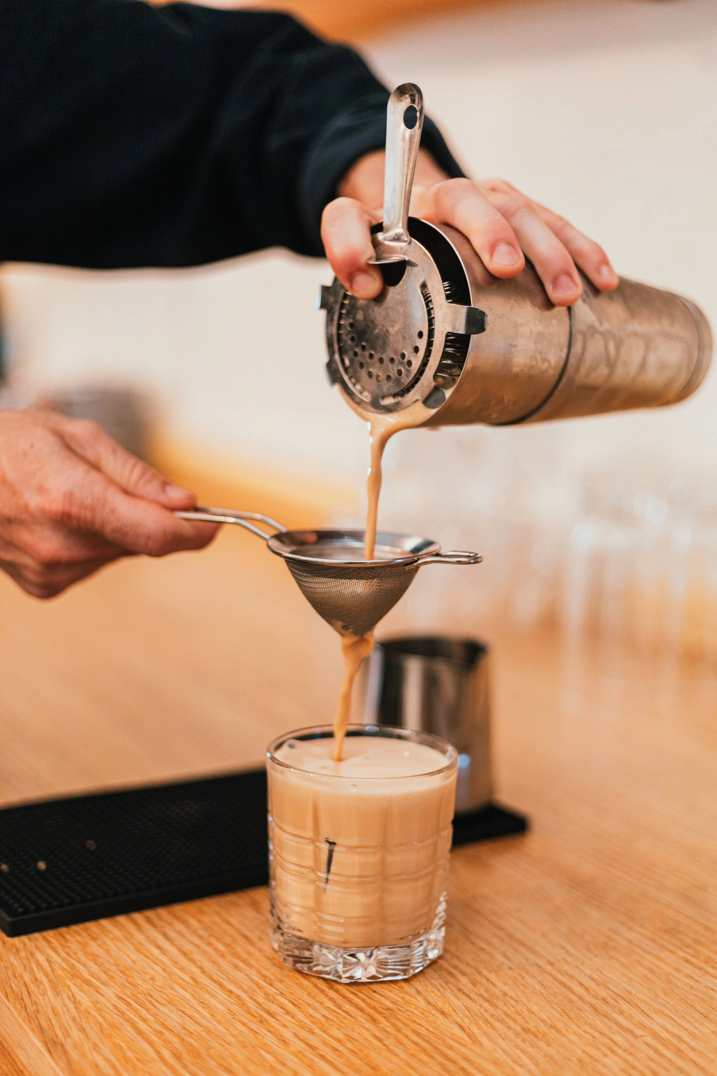 Une personne verse un café préparé à l'aide d'une machine à piston dans un verre. La scène se déroule probablement dans un café ou un bar à café.