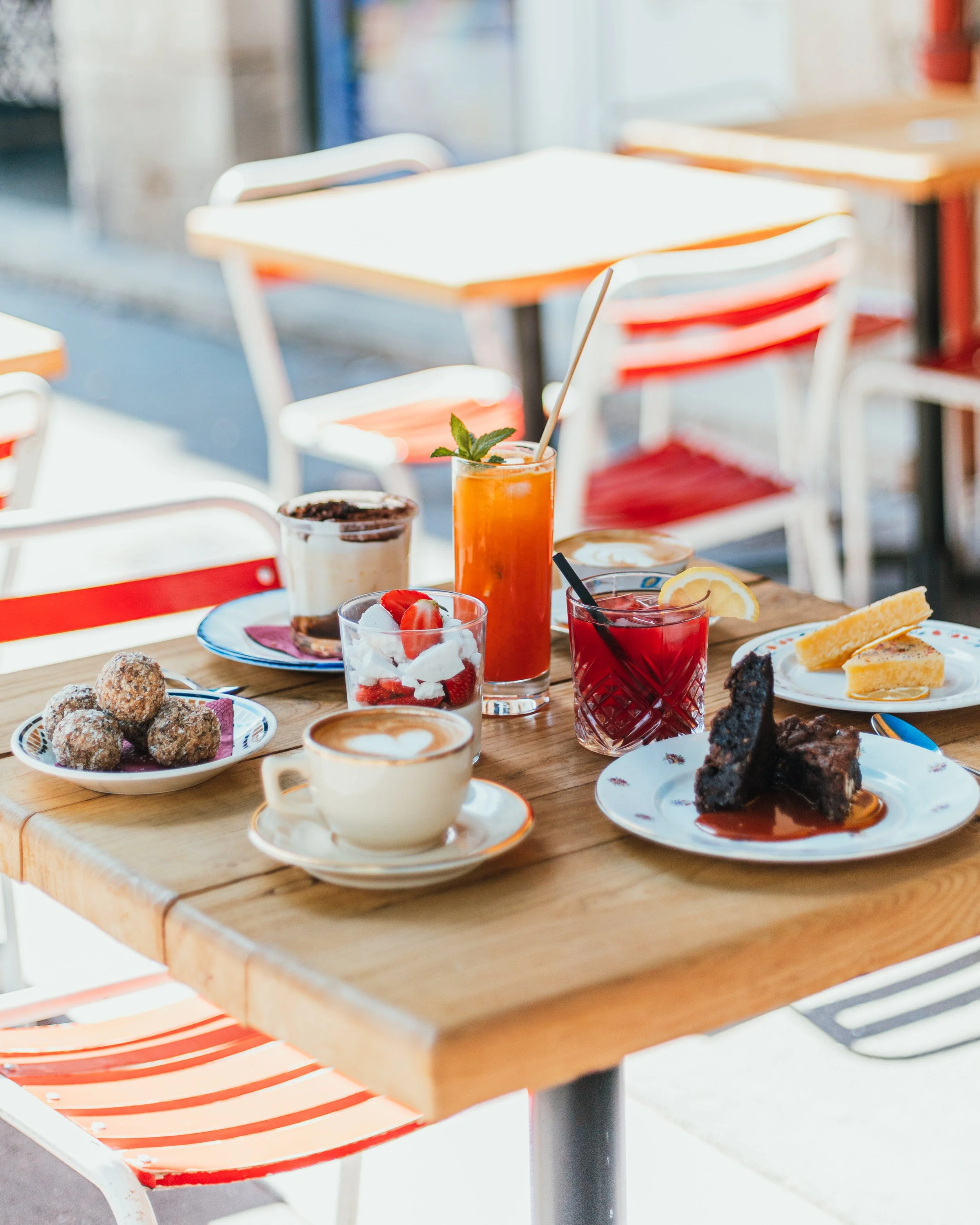 Table de petit déjeuner avec des desserts, boissons et fruits dans un café en plein air.