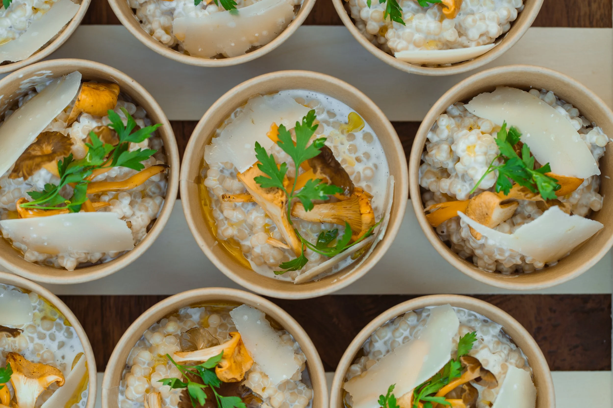Petits bols en carton contenant une salade de quinoa garnie de champignons, de copeaux de fromage, de persil et d'huile d'olive.