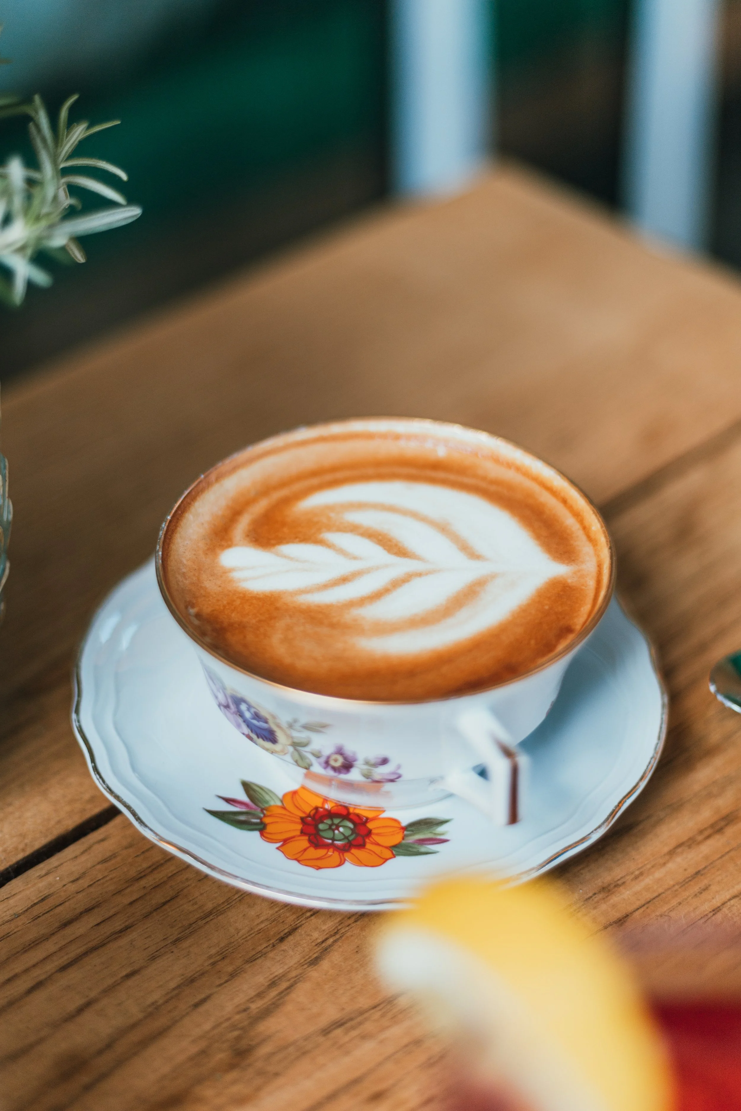 Un cappuccino avec un motif de latte art dans une tasse en porcelaine blanche avec un motif floral sur une table en bois.