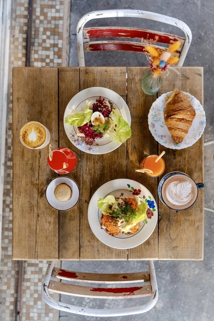 Table avec petit déjeuner comprenant une salade, un croissant, deux boissons chaudes et deux boissons froides, vue du dessus.