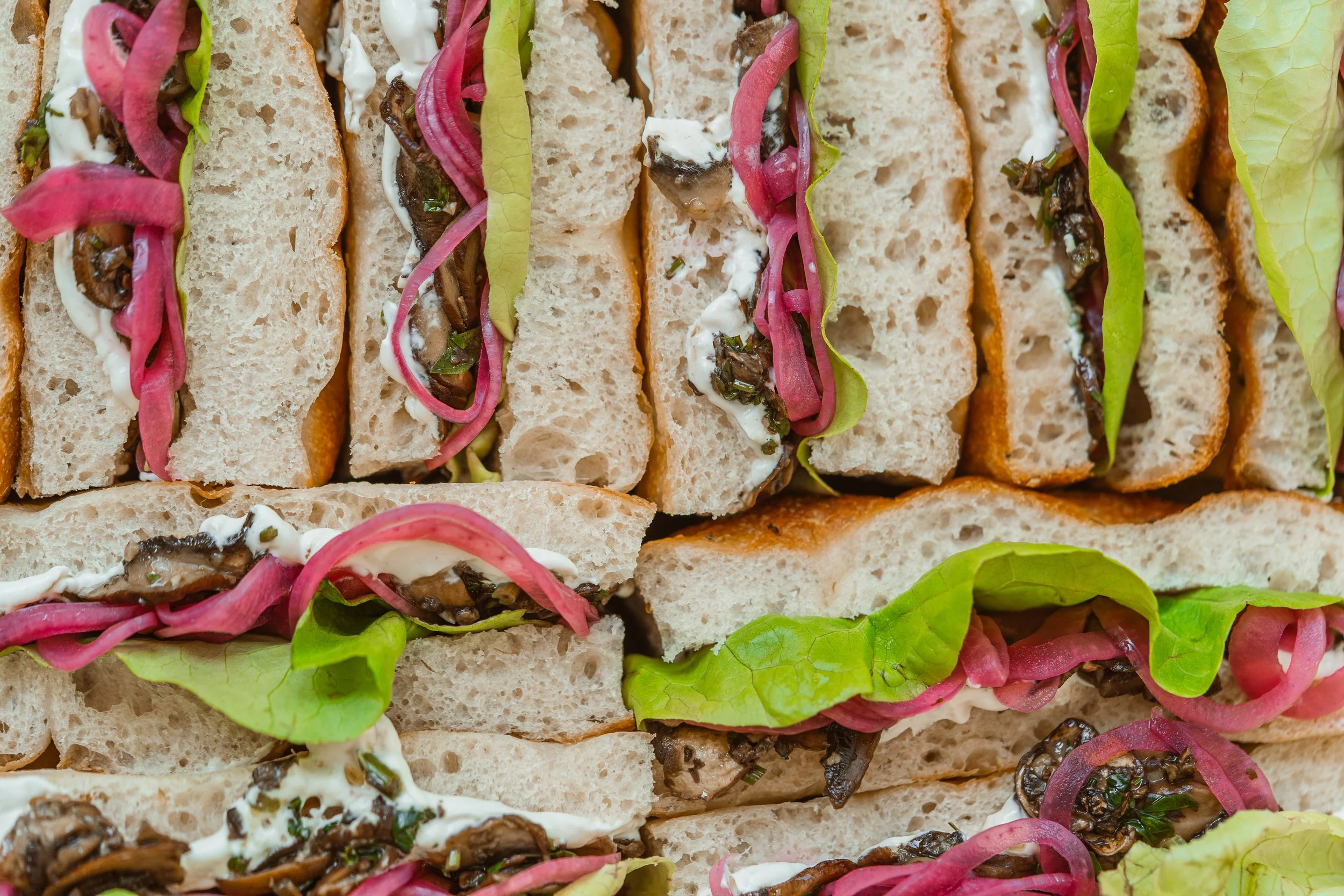 Sandwichs avec du pain focaccia, de la salade, des oignons rouges, et une sauce ou un fromage