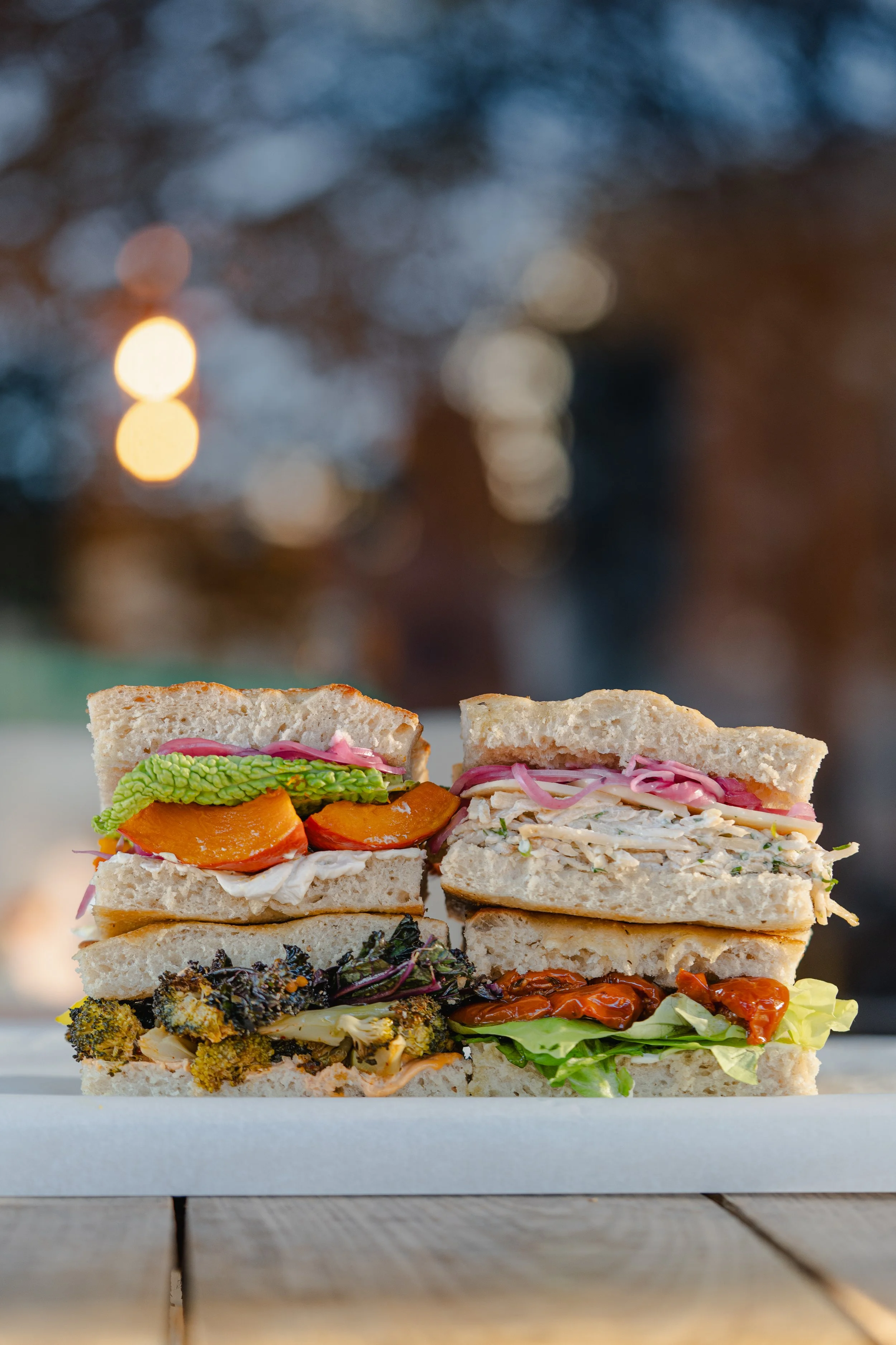 Deux sandwiches multi-délices avec des légumes et des viandes sur une surface en bois.
