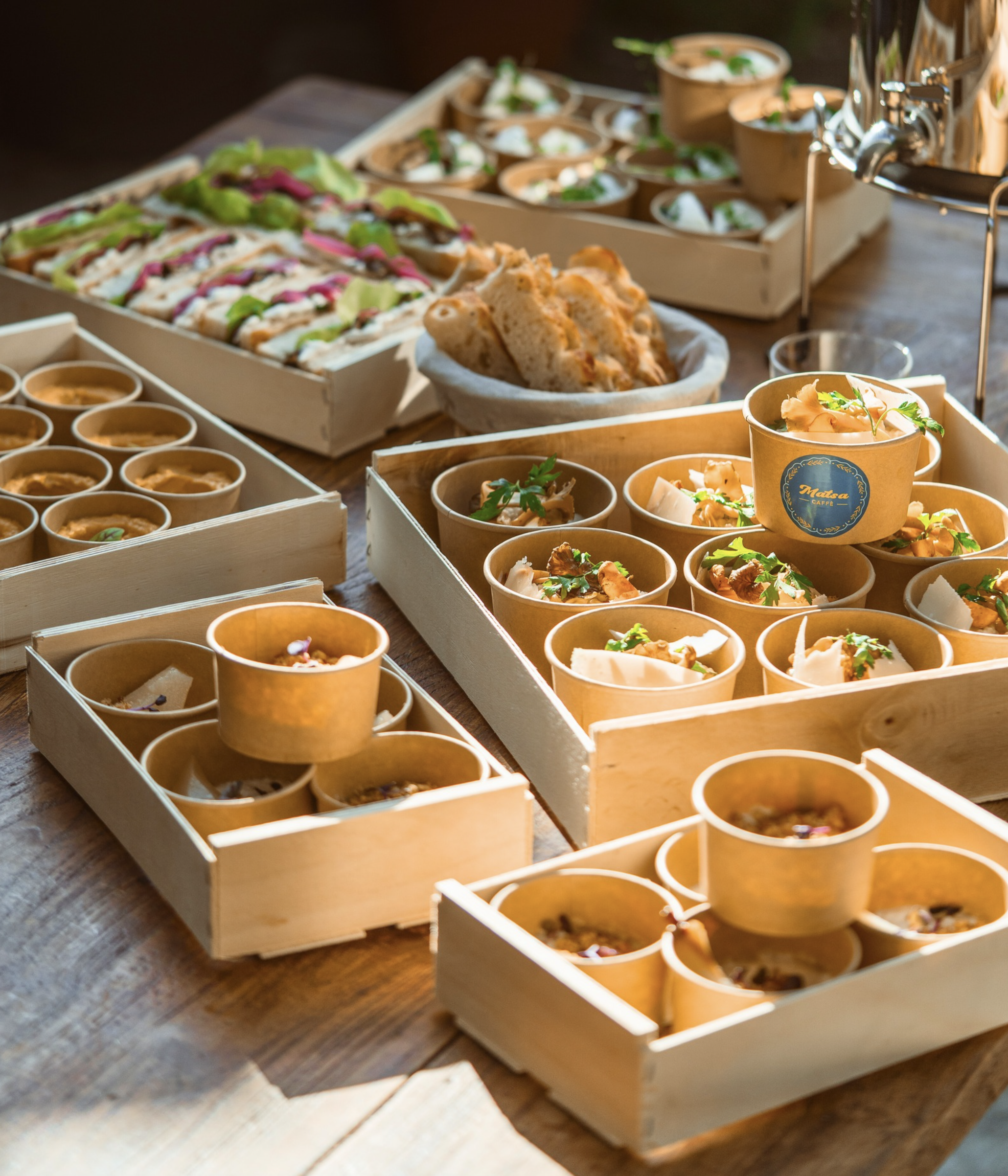 Divers plats de nourriture présentés dans des petits bols et des cartons en bois, notamment des dips, des échantillons de pain, et des garnitures pour des wraps ou tacos sur une table en bois.