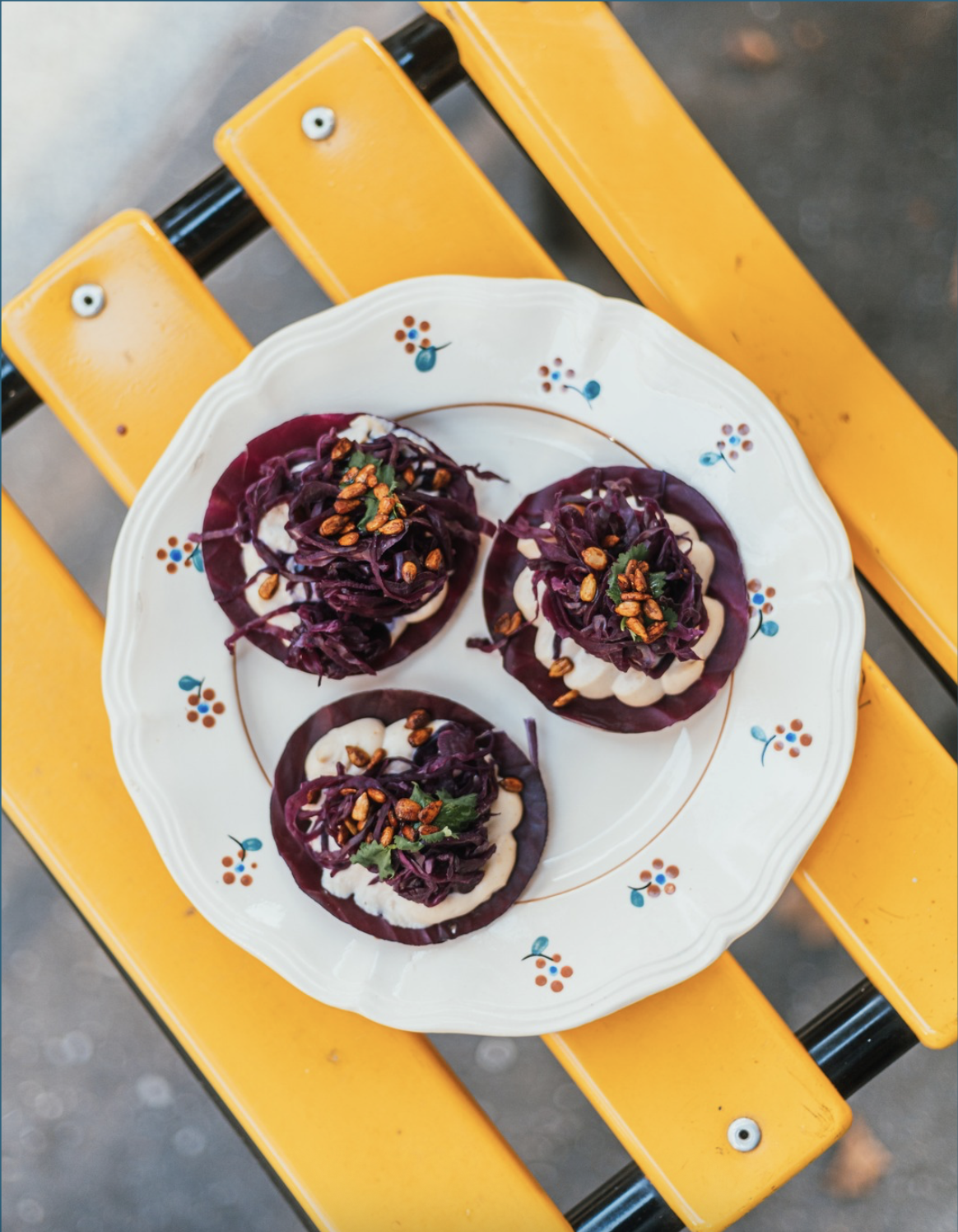Une assiette avec trois amuse-bouches configurés de façon artistique, garnis de choux rouges, de noisettes et de crème.