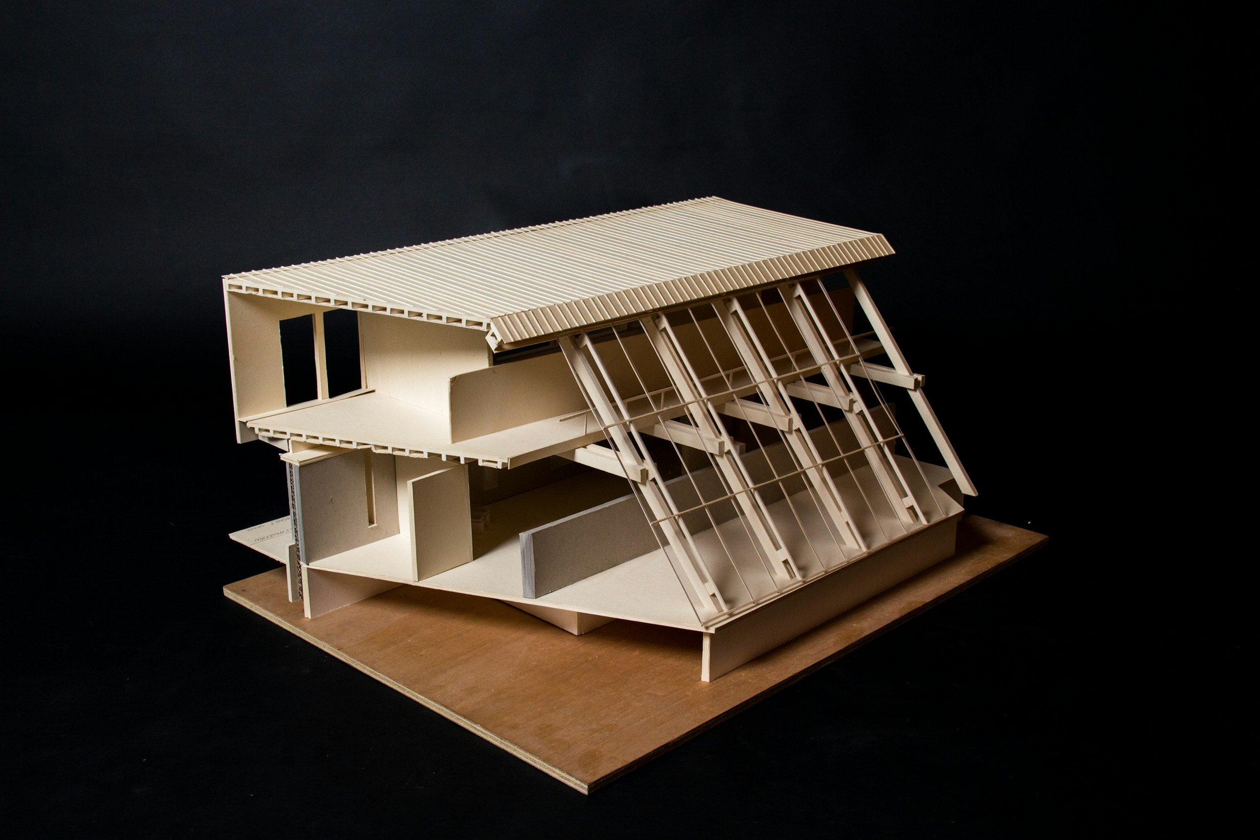 Architectural model of a modern multi-story building with large glass windows and a sloped roof, set on a wooden base.