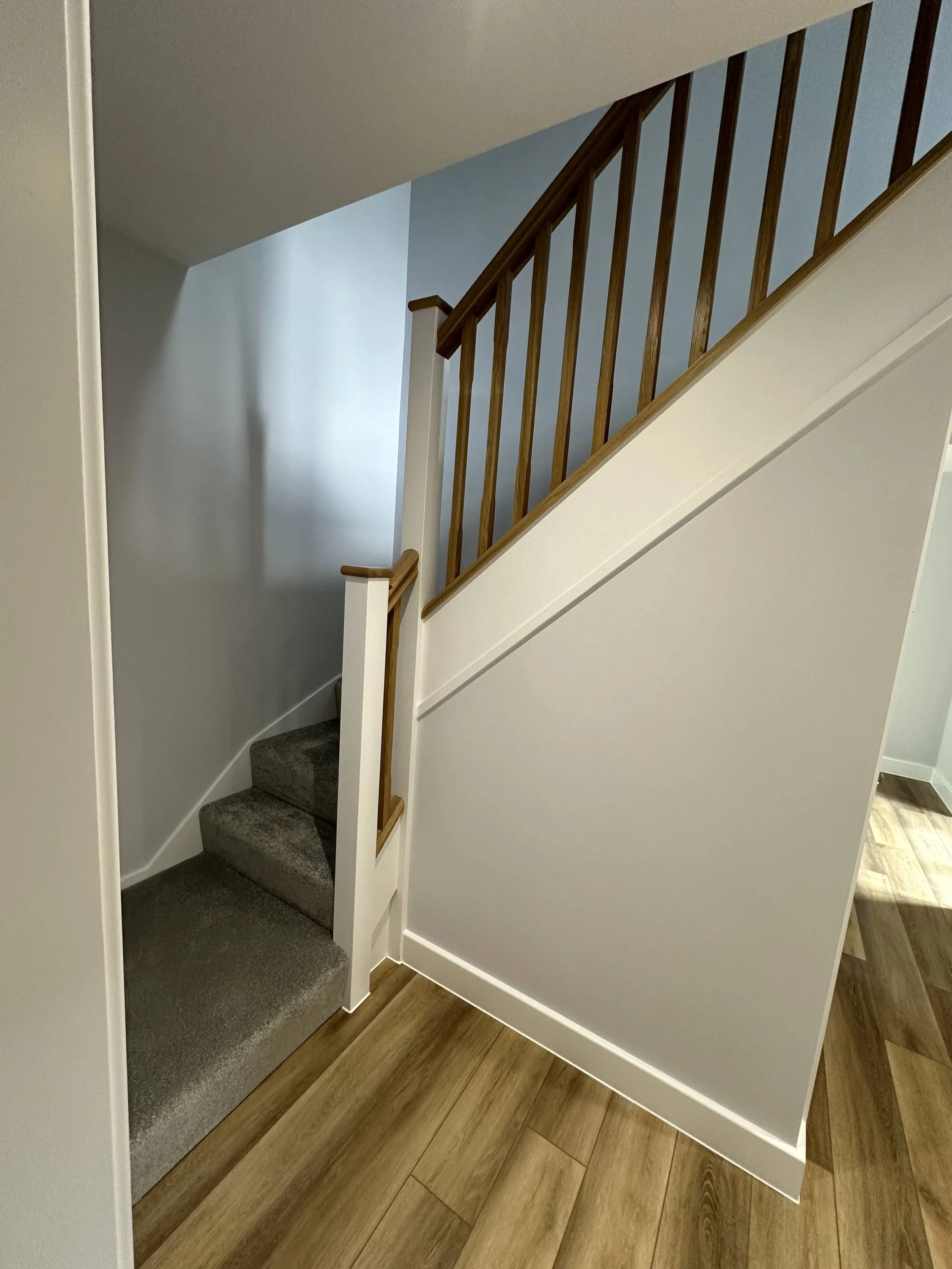 Interior view of a staircase with carpeted steps, wood balcony railing, and wood flooring.