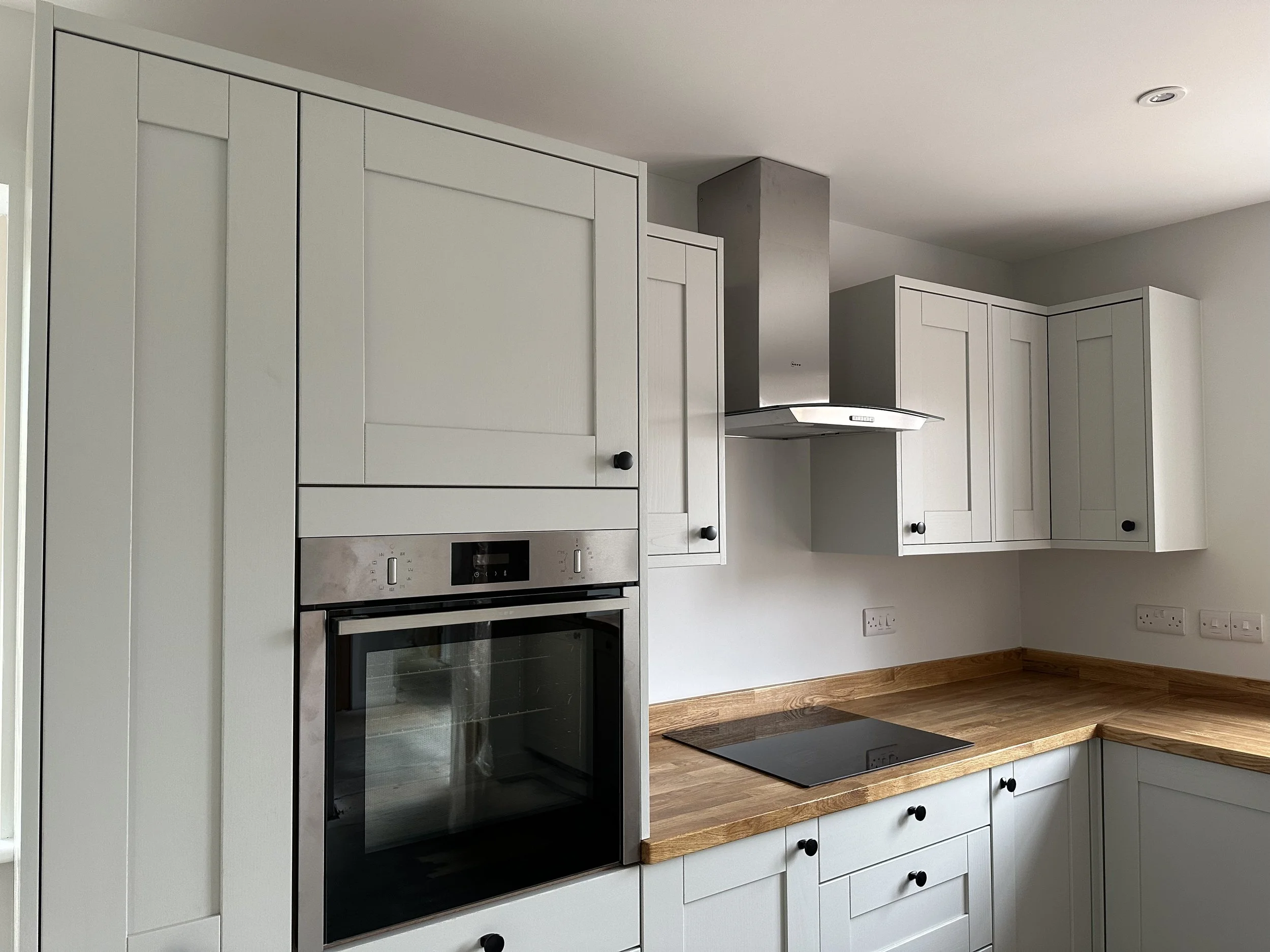 Modern kitchen with white cabinets, wooden countertop, built-in oven, and stovetop, stainless steel range hood, and multiple electrical outlets
