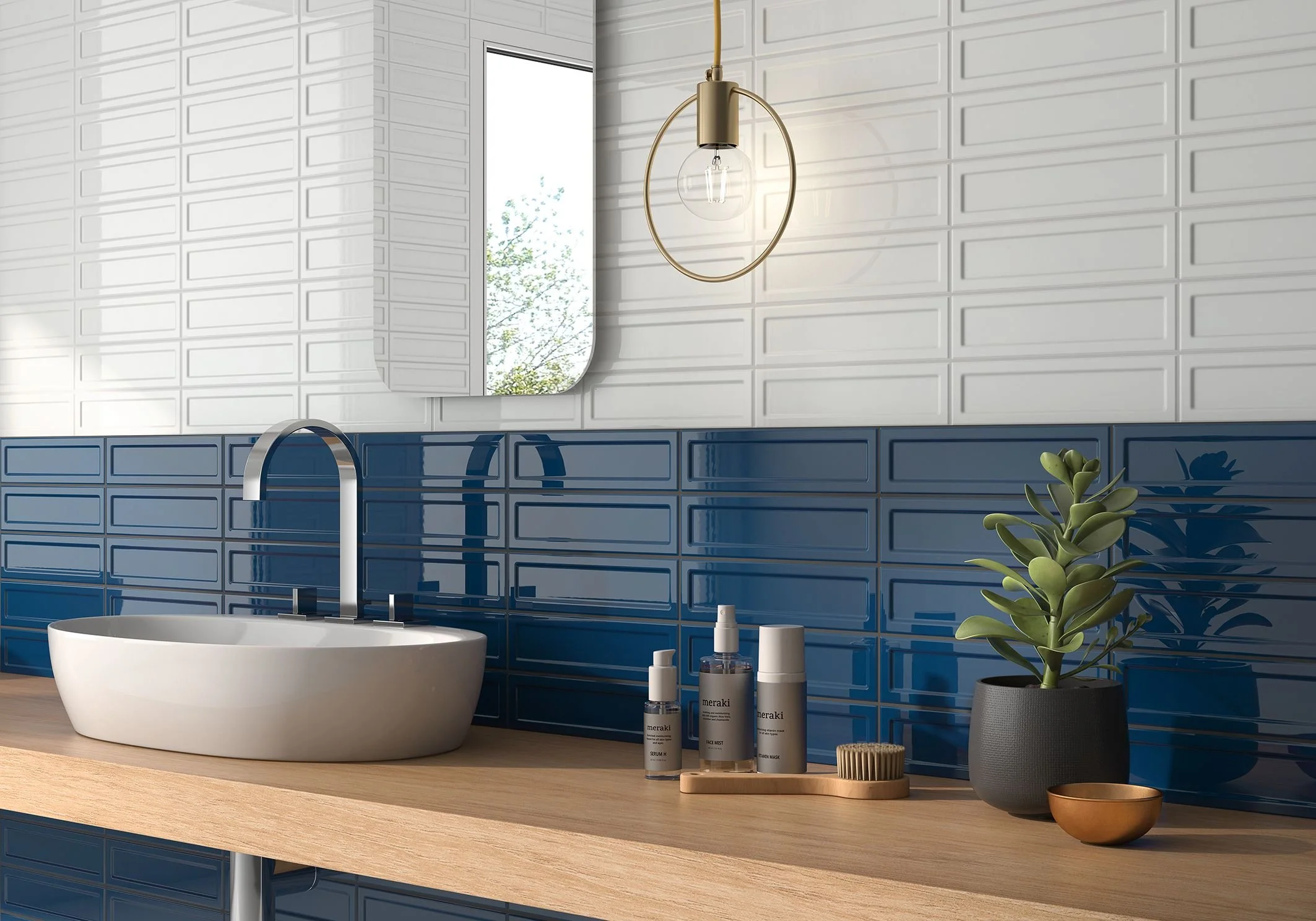 Modern bathroom with white and blue tiled walls, a wooden countertop, a white oval sink, bottled skincare products, a small plant in a black pot, a mirror, a window, and a gold wall sconce.