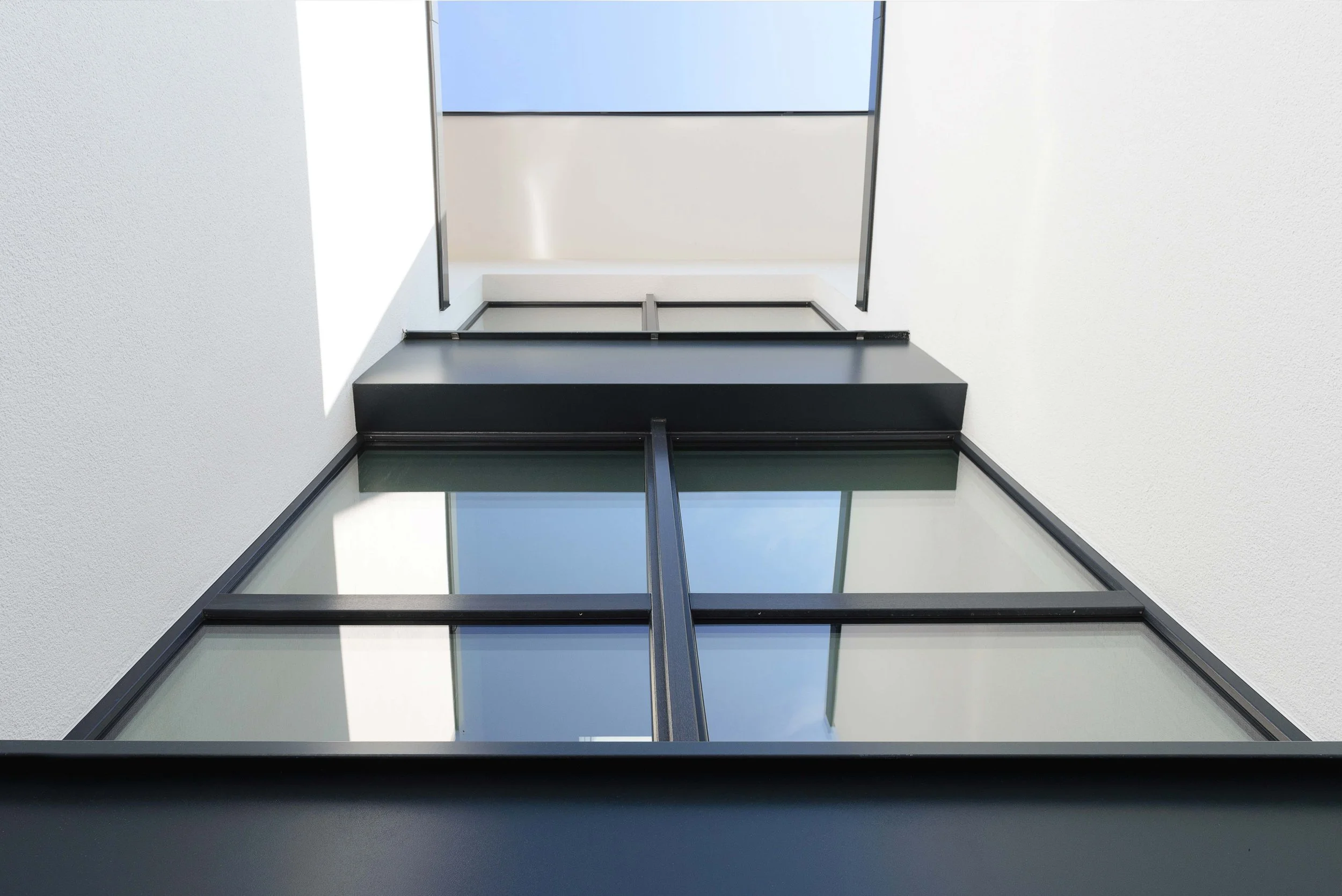 Blick nach oben auf die moderne Gebäudefassade mit großen Glasfenstern und weißer Wand