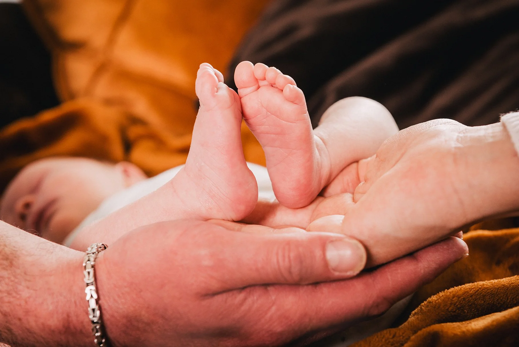 Nahaufnahme eines Neugeborenen, das in den Händen eines Erwachsenen liegt, mit Fokus auf die winzigen Füße des Babys.