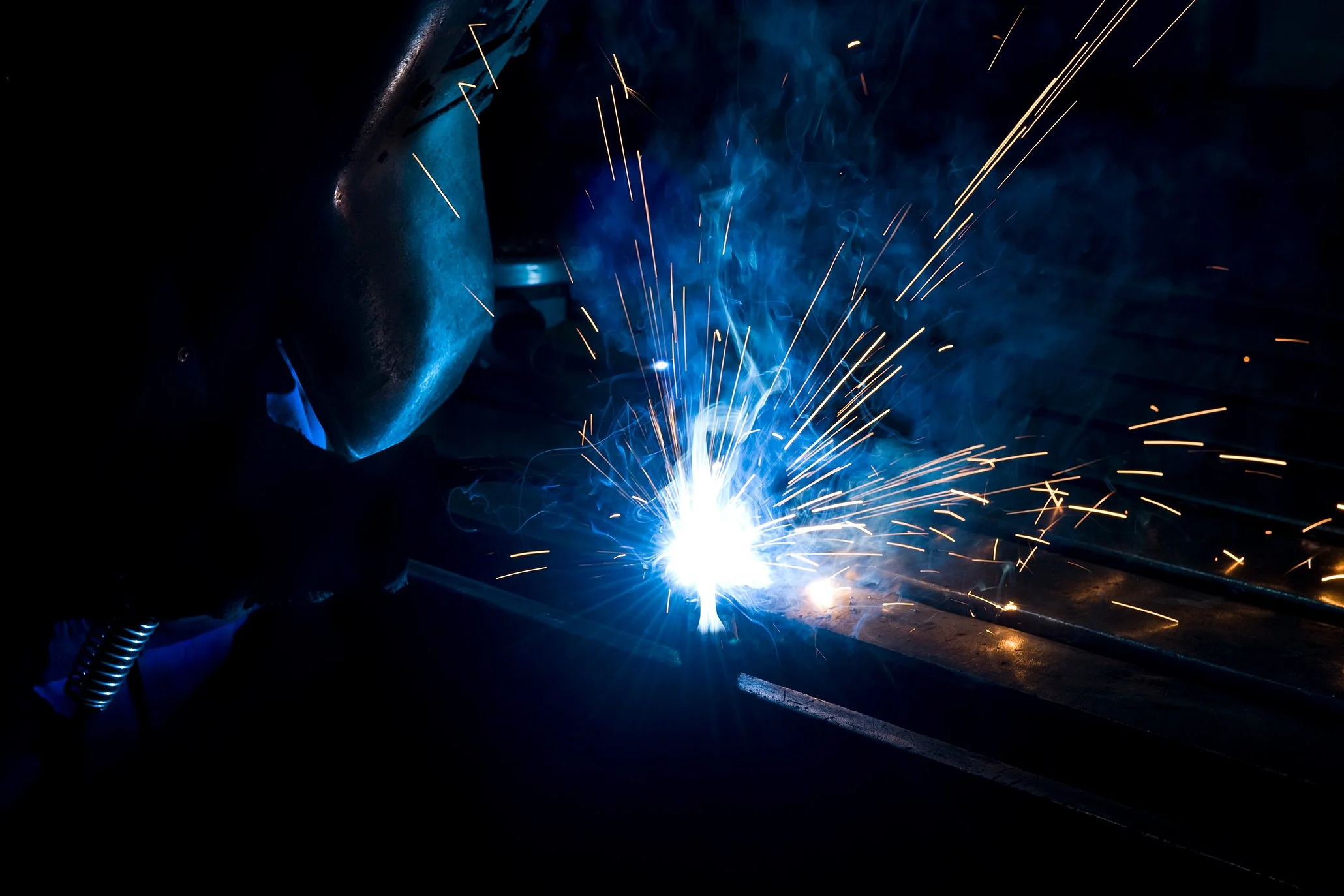 Schweißer bei der Arbeit, mit Funkenflug und blauer Flamme
