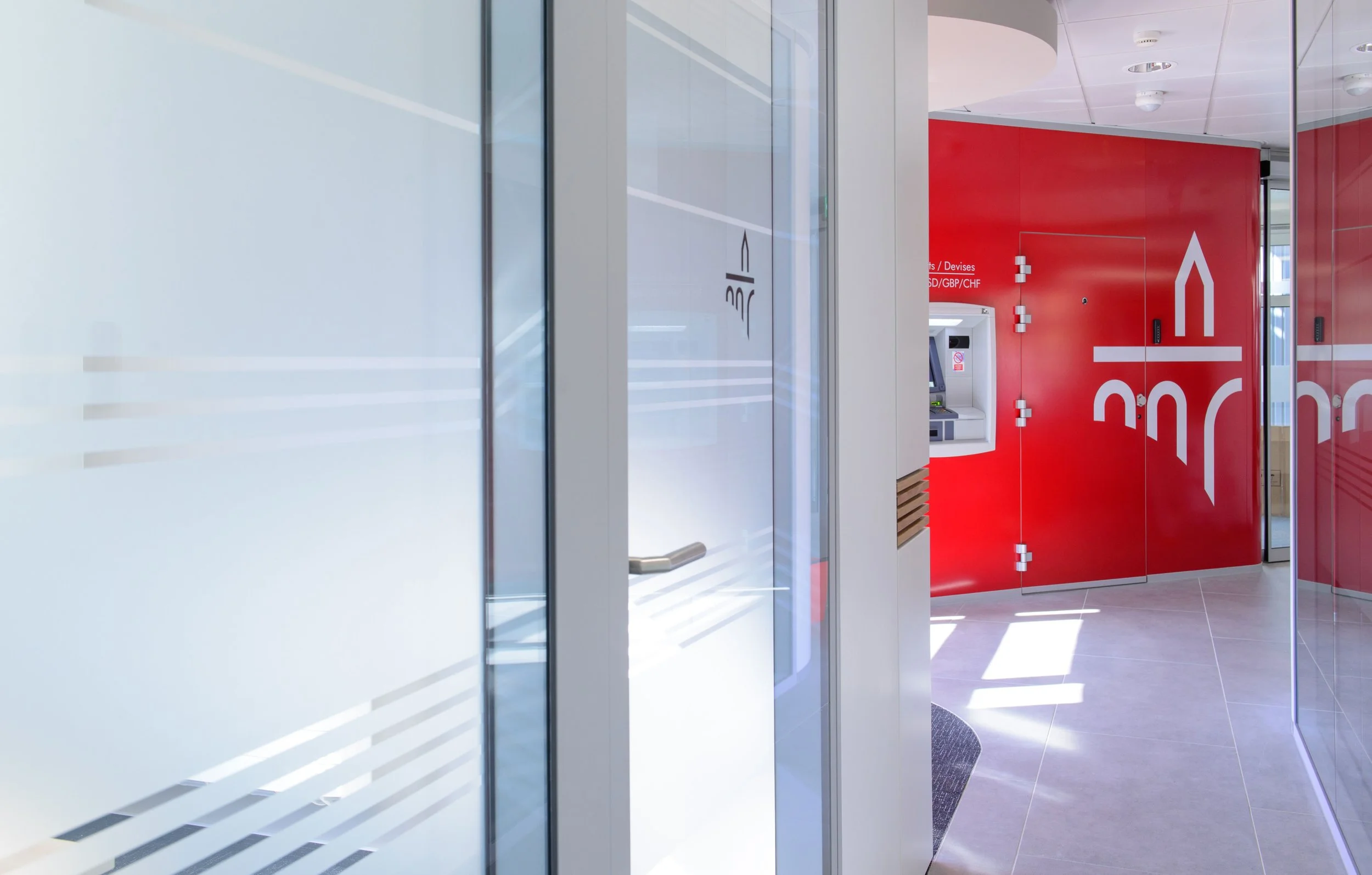 Moderner Bankautomat vor roter Wand in einem öffentlichen Innenraum.