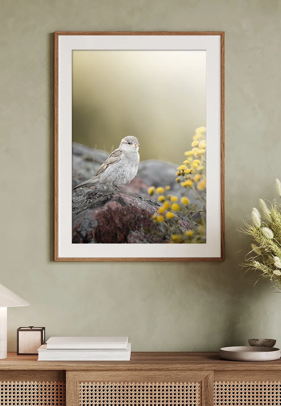 Ein Wandbild eines kleinen Vogels auf einem Felsen, mit verblasstem Hintergrund und gelben Blüten im Vordergrund.