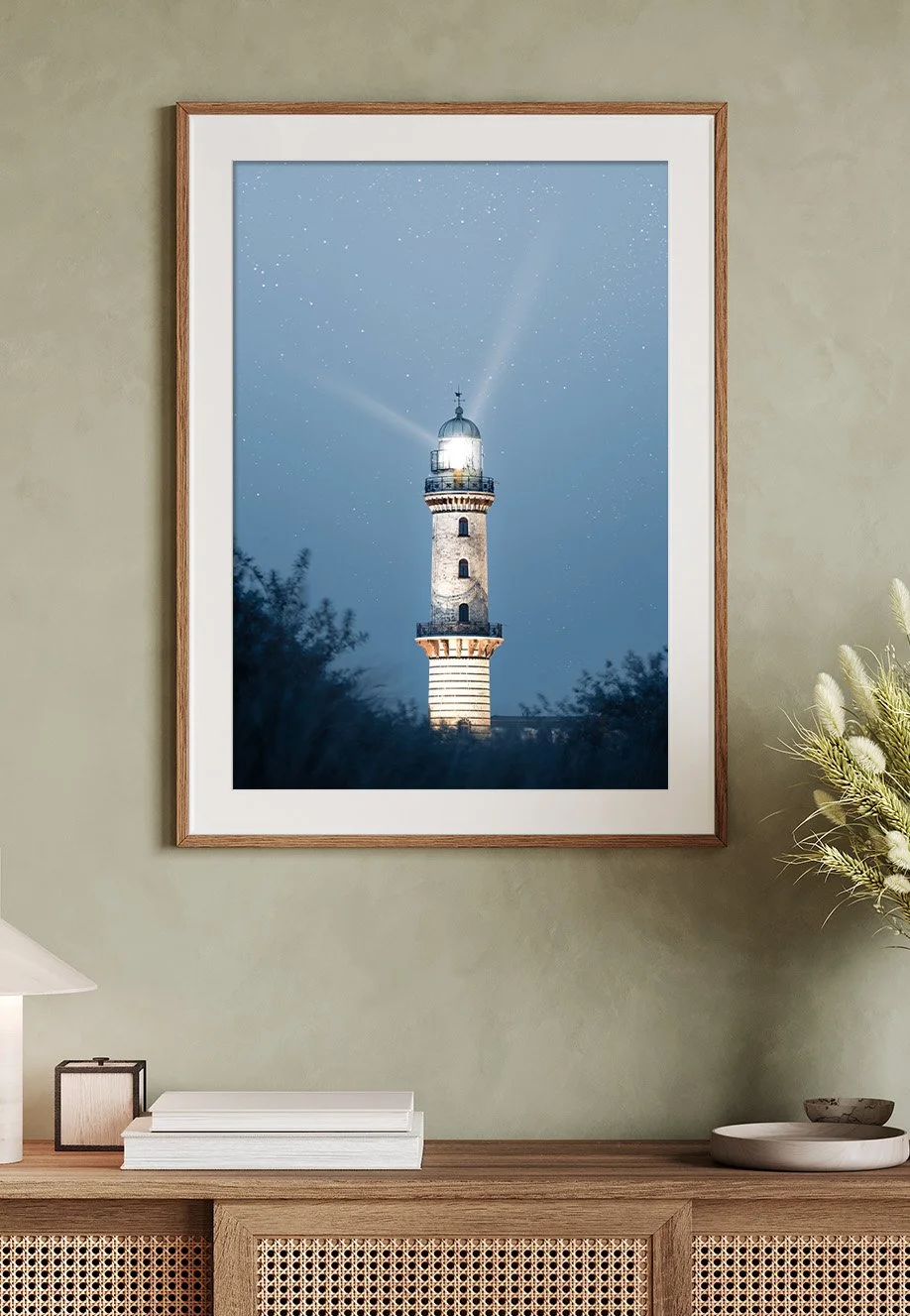 Ein Leuchtturm in Warnemünde, Deutschland bei Nacht mit strahlendem Licht und Sternenhimmel im Hintergrund.