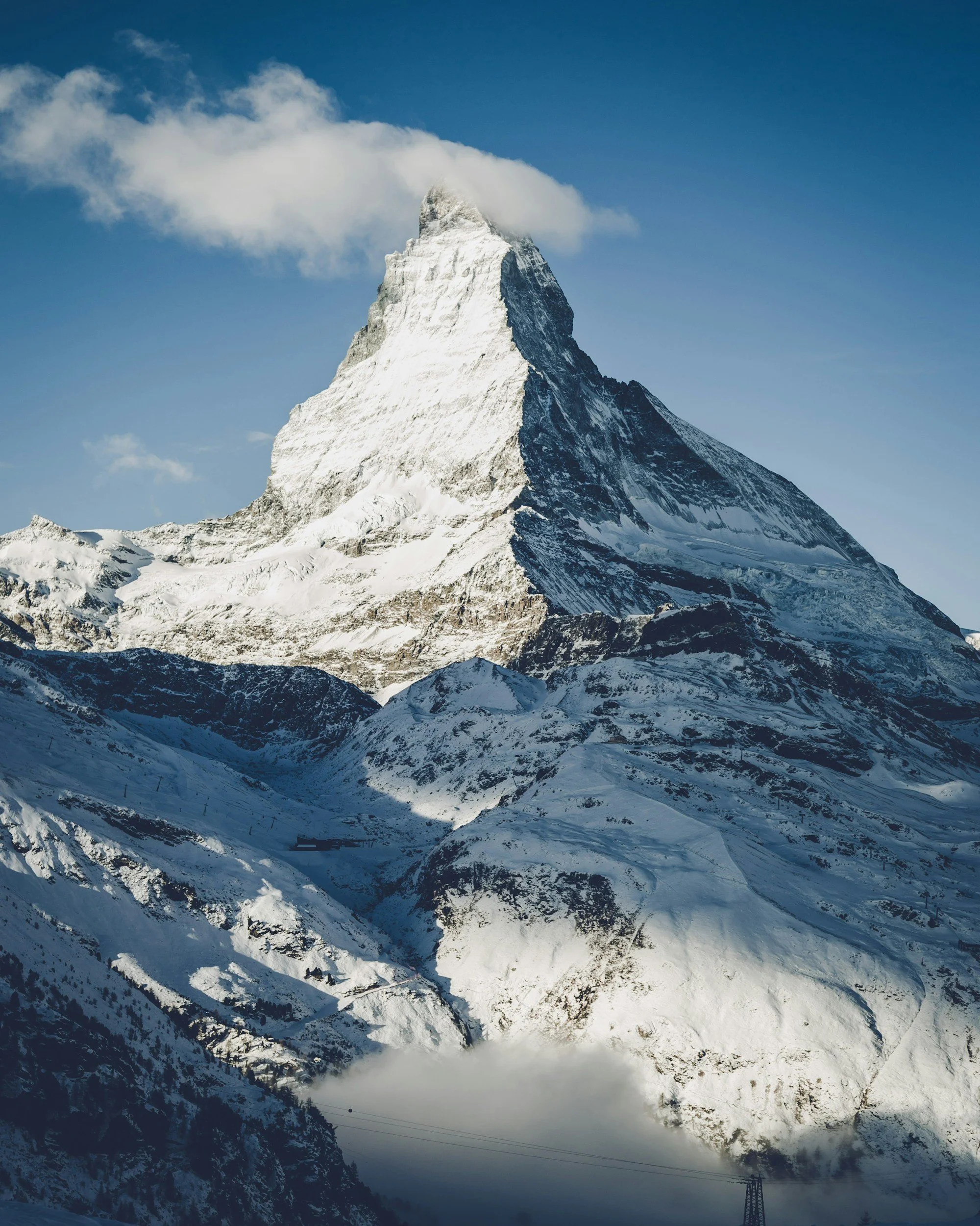 Snow-covered mountain peak rising above snowy slopes and a blue sky with a few clouds.